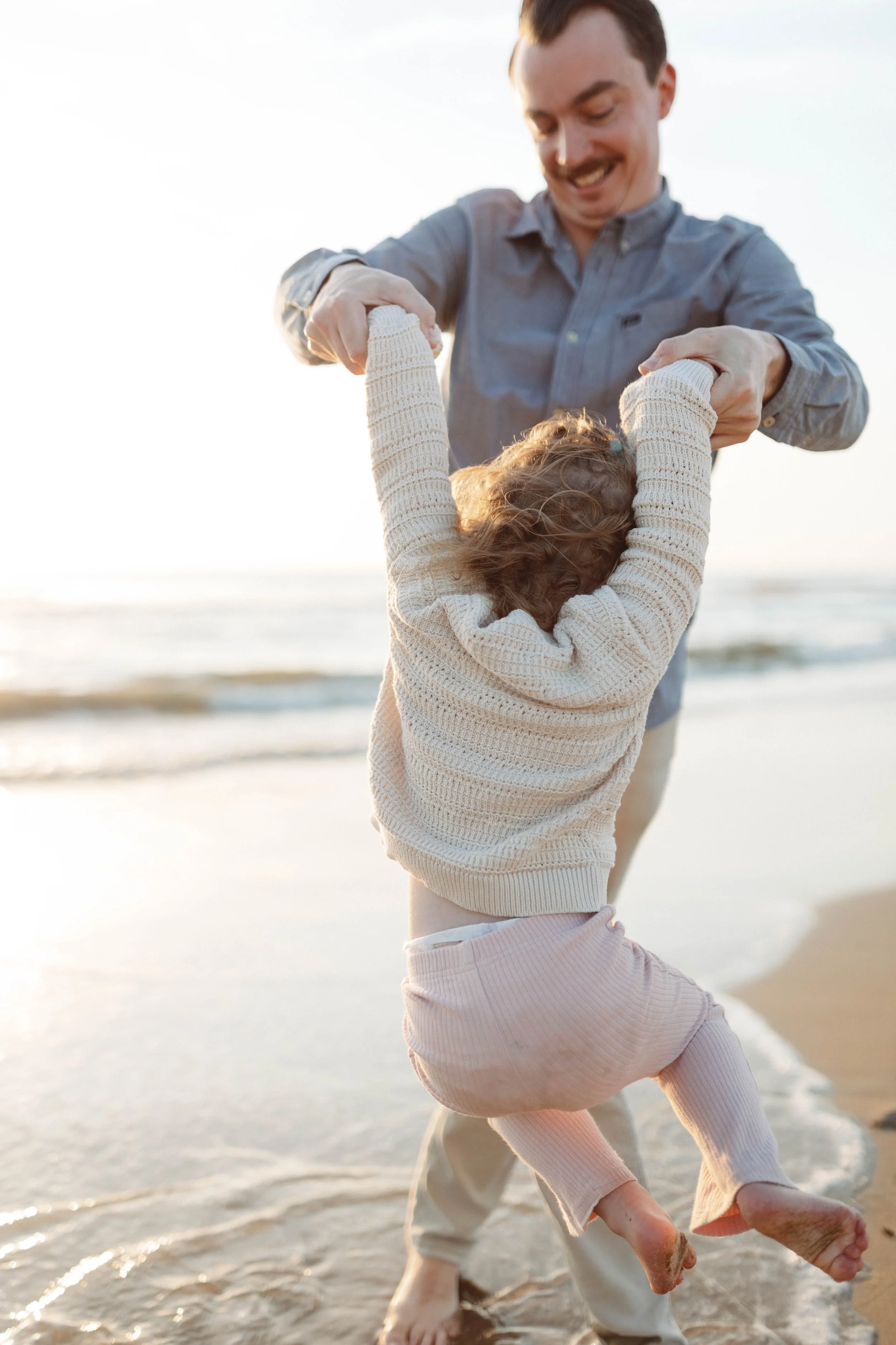 man holding toddlers hands smiling and swinging little girl around