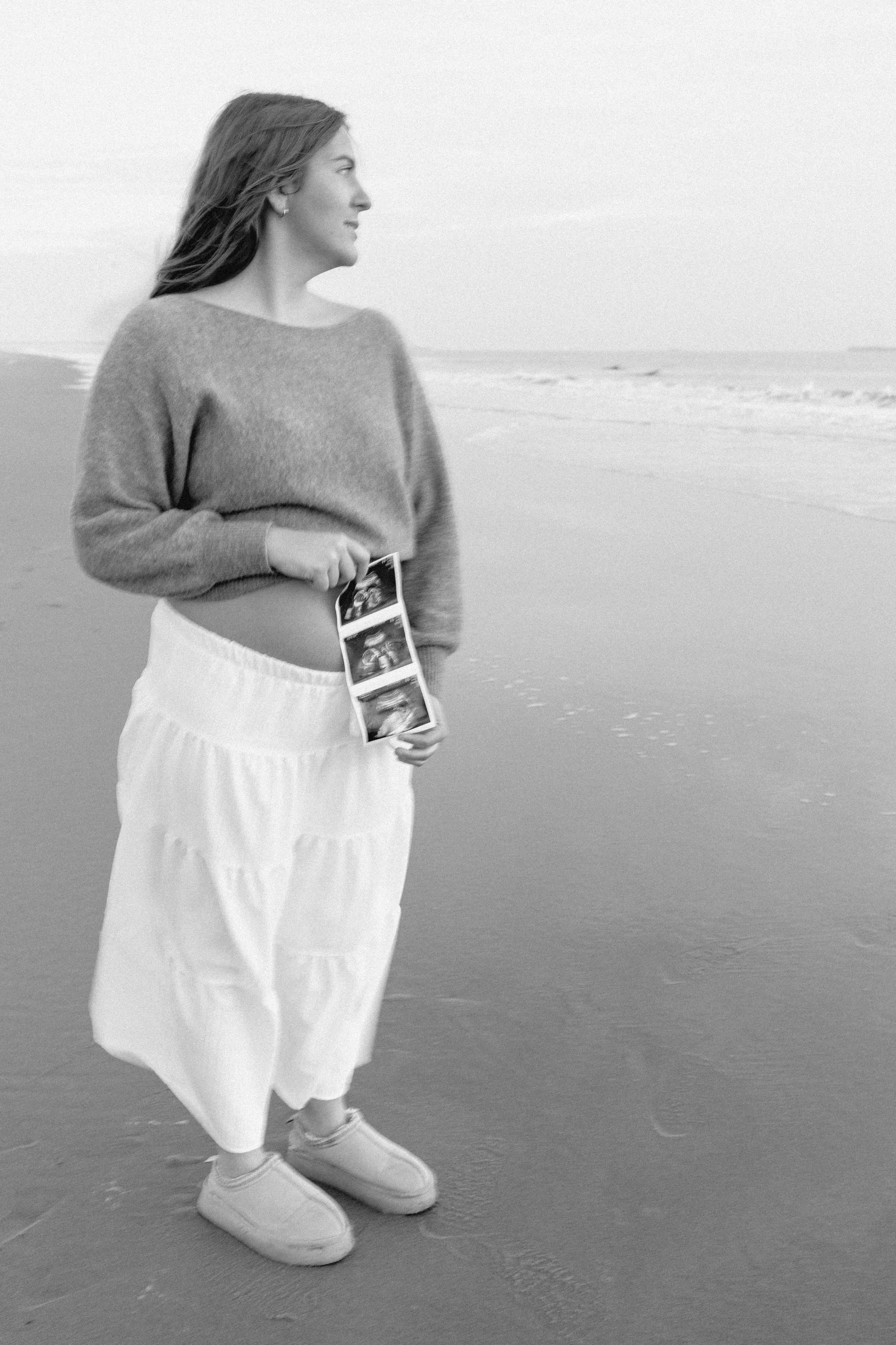 black and white image of woman holding ultrasound strip looking out at the ocean