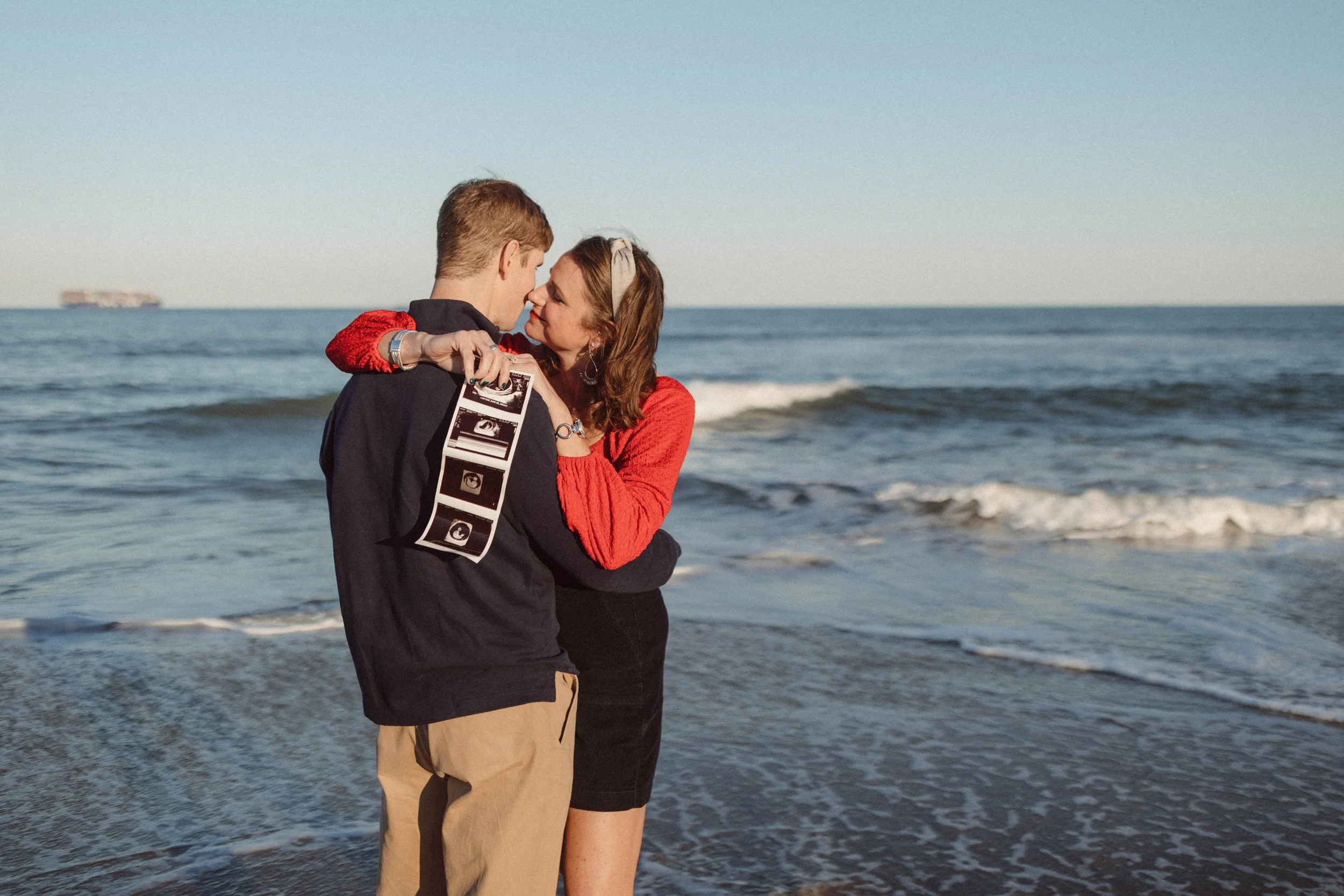 Married couple holds ultrasound picture standing in front of Ocean in Virginia Beach Virginia