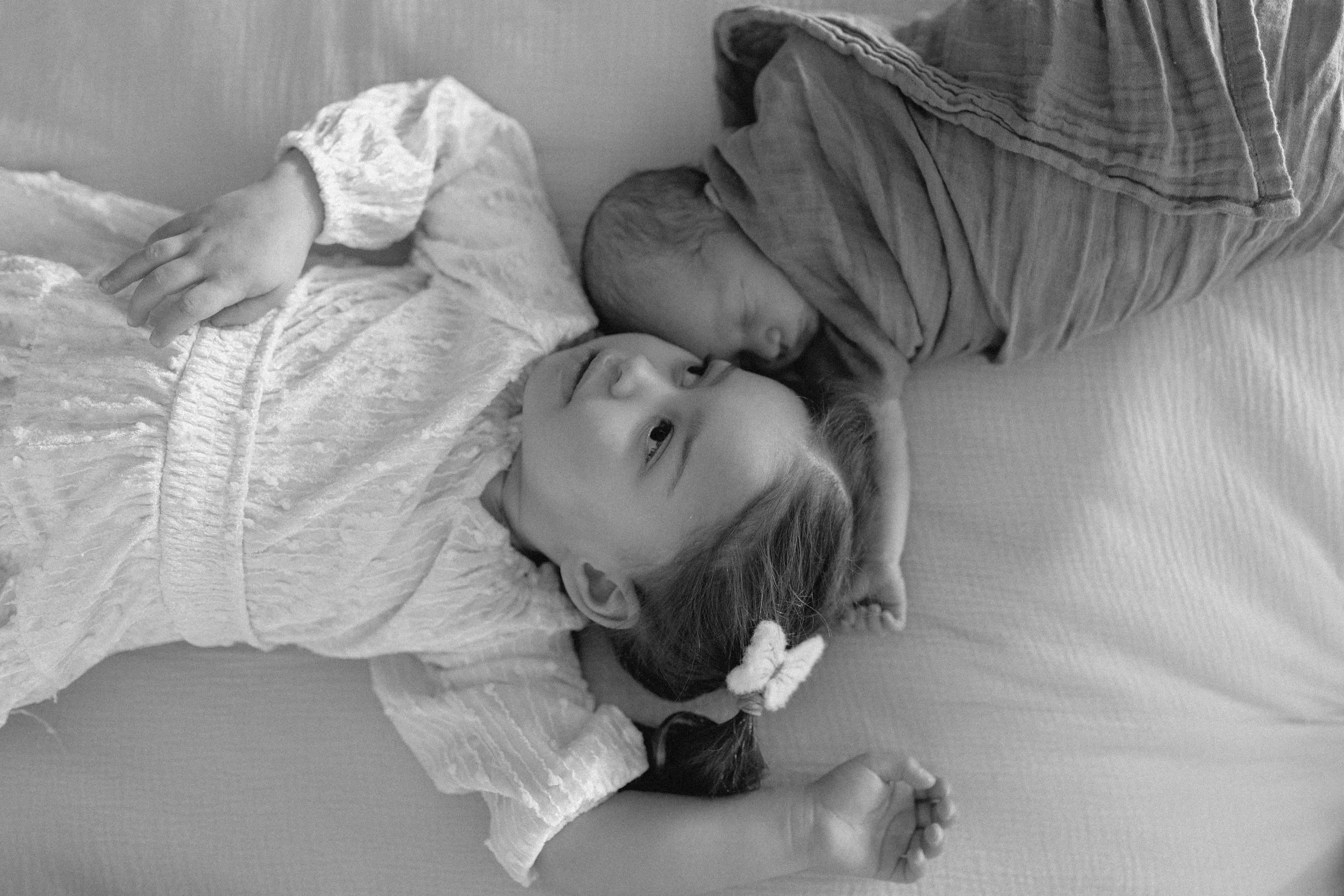 toddler and children in black and white image lay on bed and look at each other