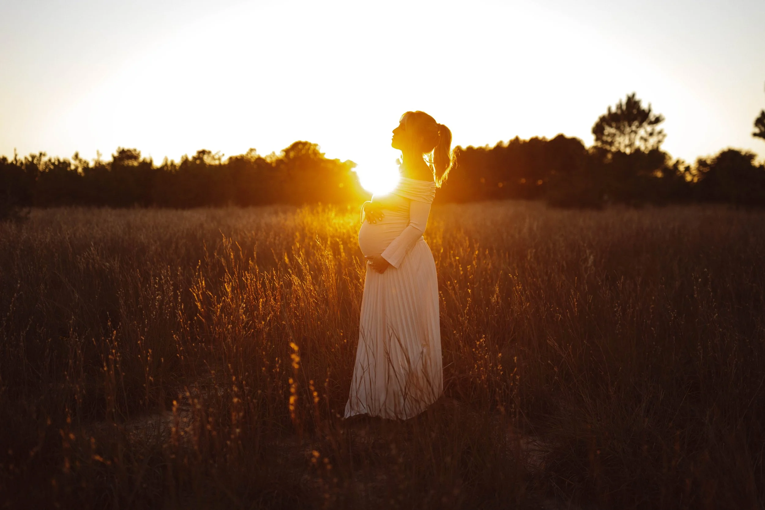 Golden hour maternity photography featuring pregnant woman silhouetted against sunset