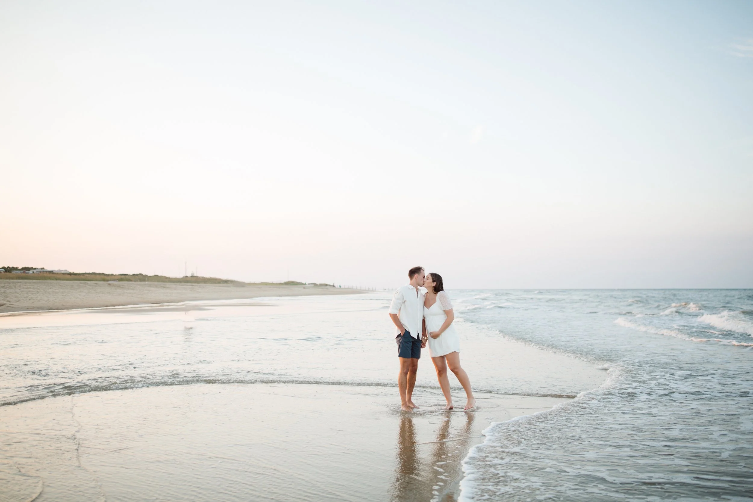 A couple standing on the beach at sunset, embracing and touching foreheads with the ocean behind them.