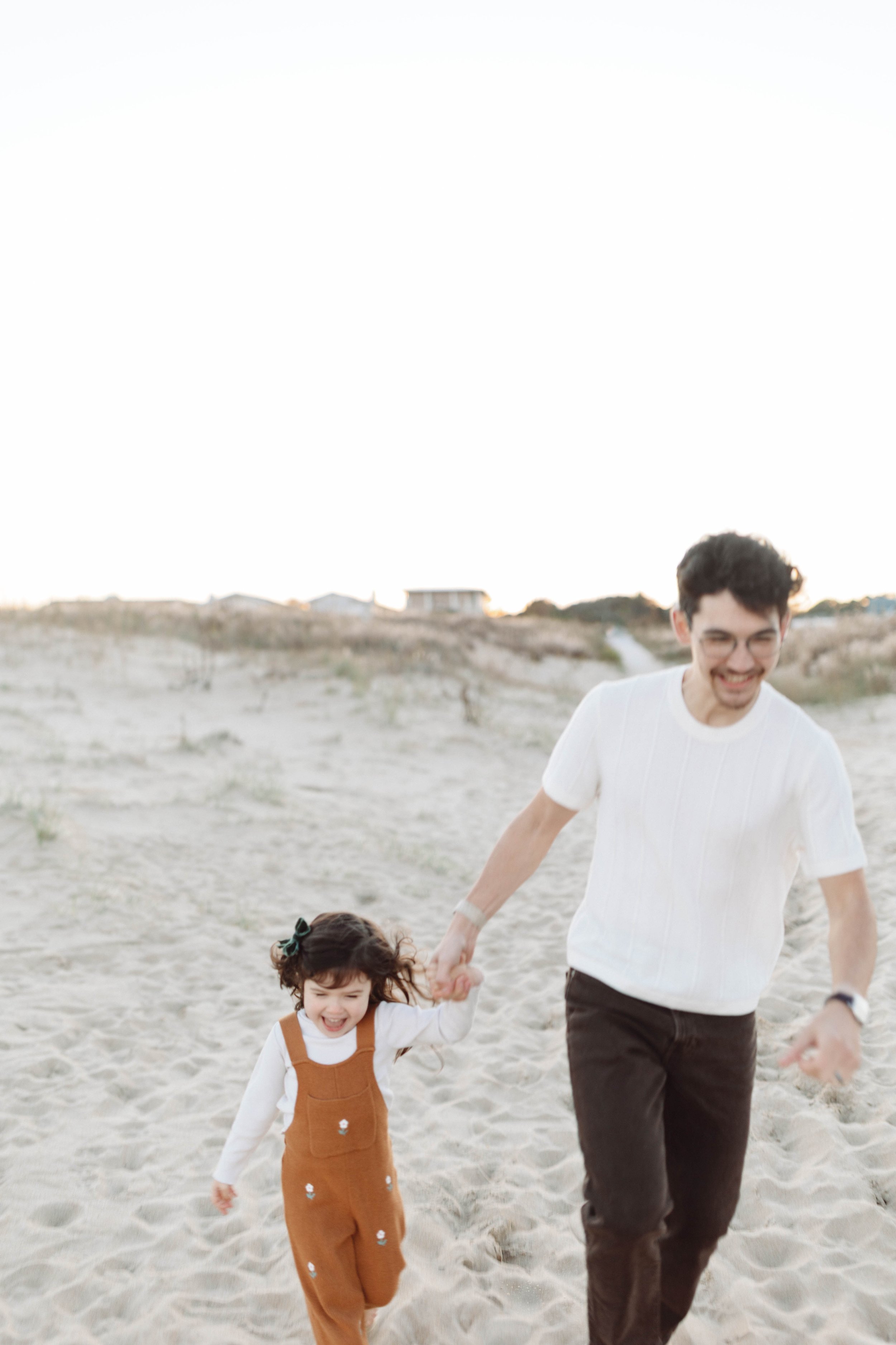 A smiling man and young girl holding hands, running on a sandy beach during daytime.