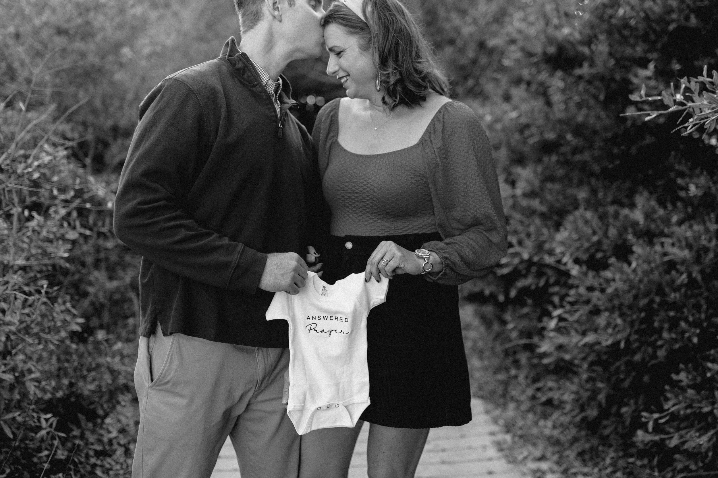 virginia beach navy couple holds miracle baby onesie standing at virginia beach north end