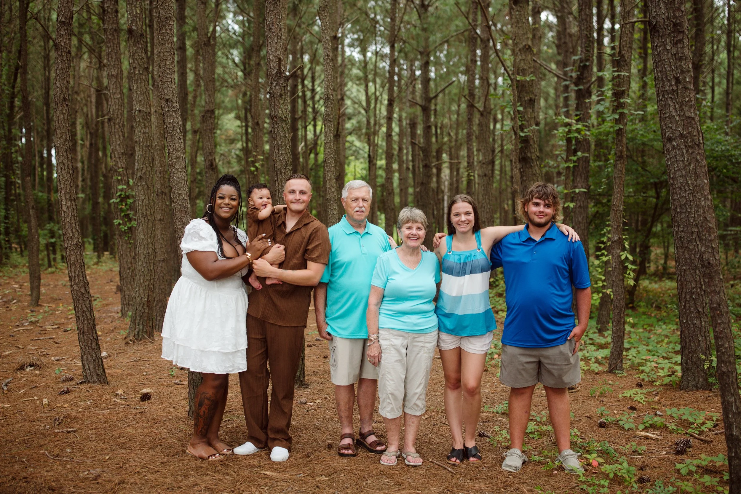Family group standing together outdoors in a forest, including adults and children smiling for the camera.