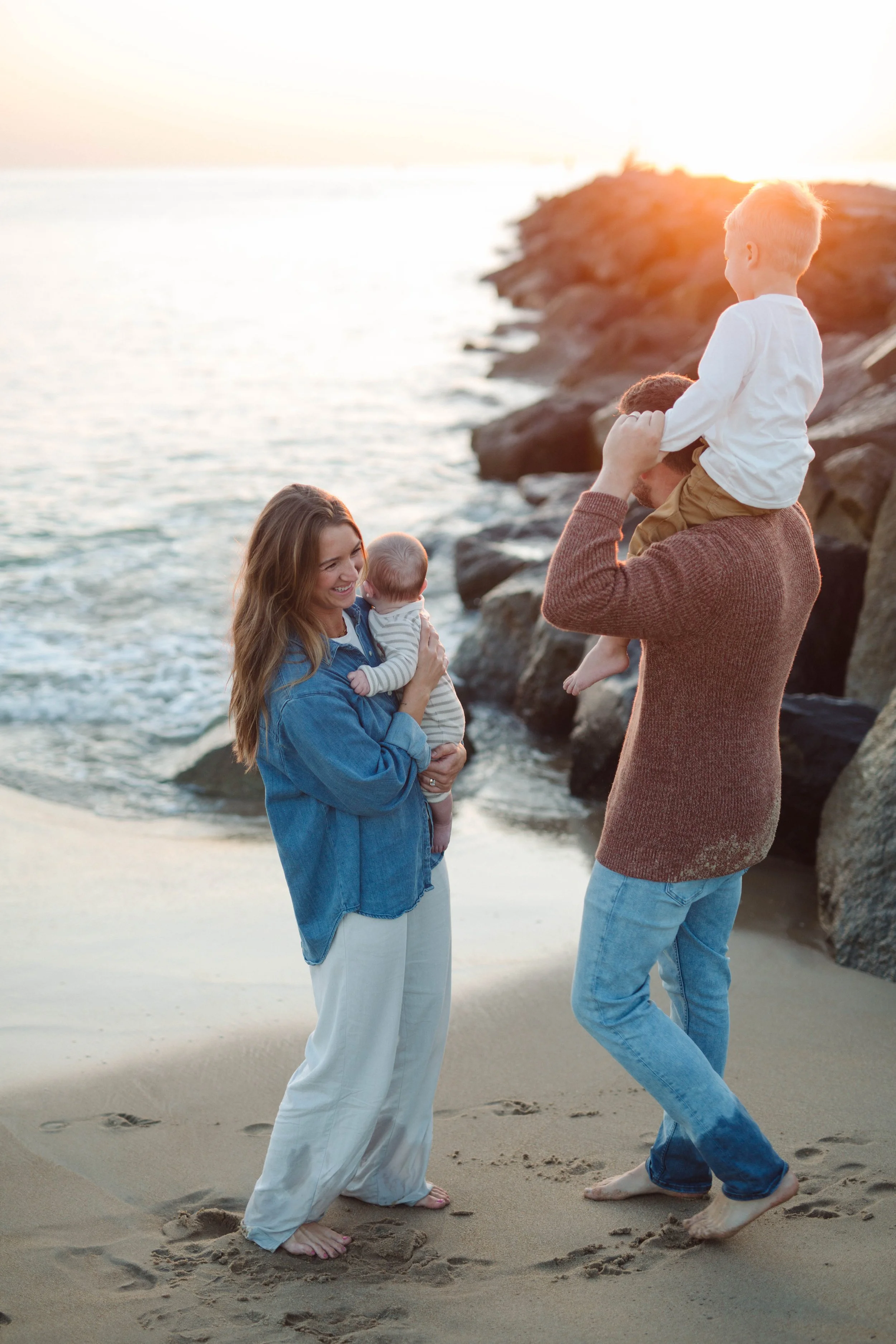 young couple stands with two children by rock formation at the Virginia Beach oceanfront during sunrise