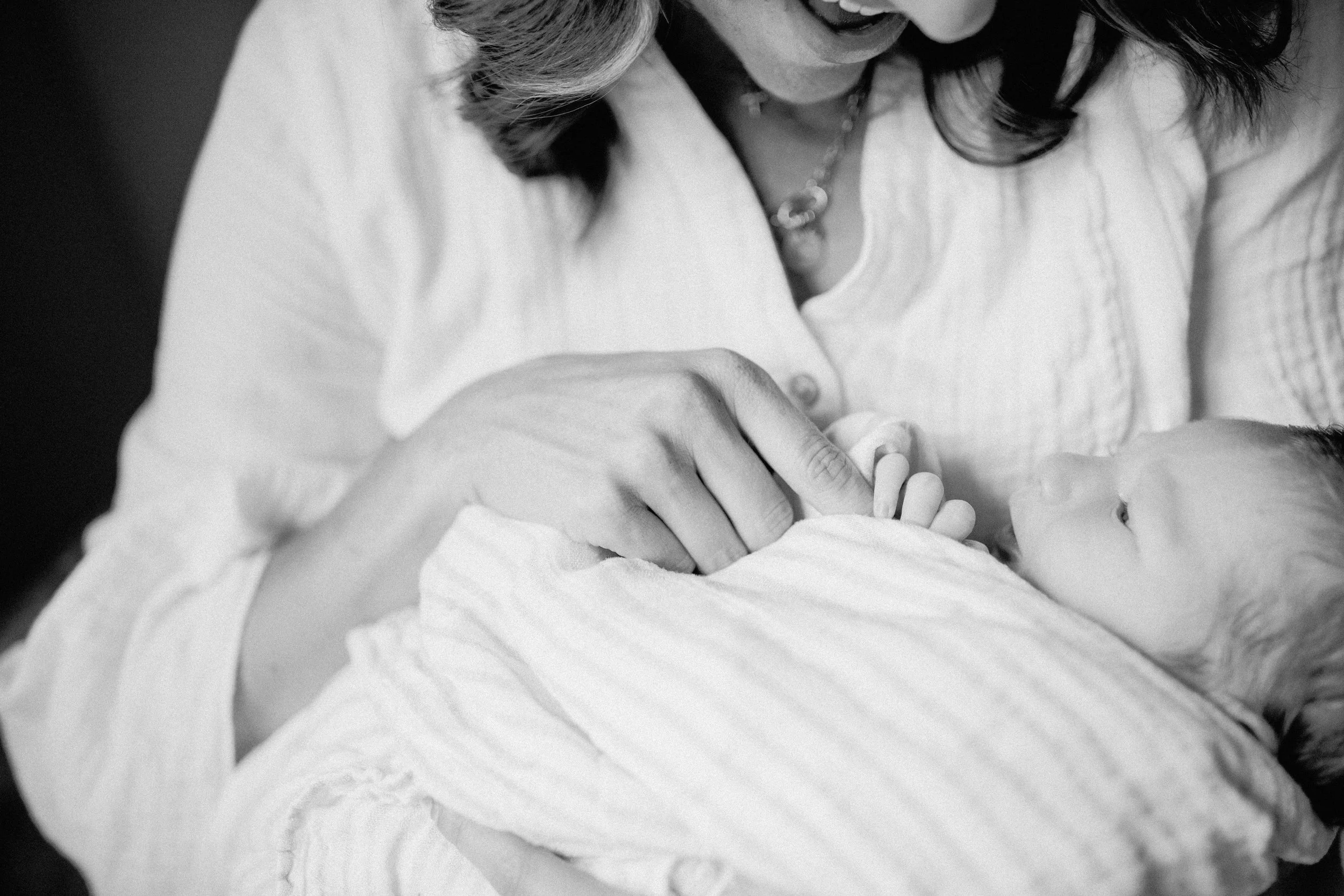A woman holding a newborn baby in her arms, smiling and looking at the baby.