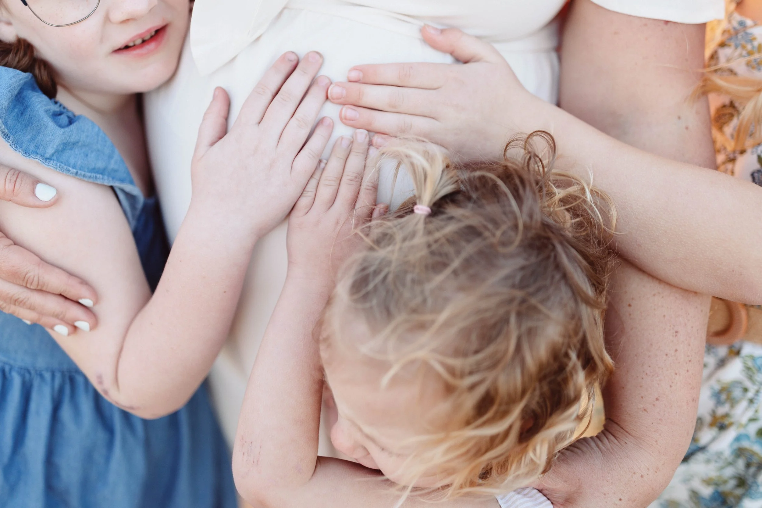three sets of childrens hands hug a pregnant belly