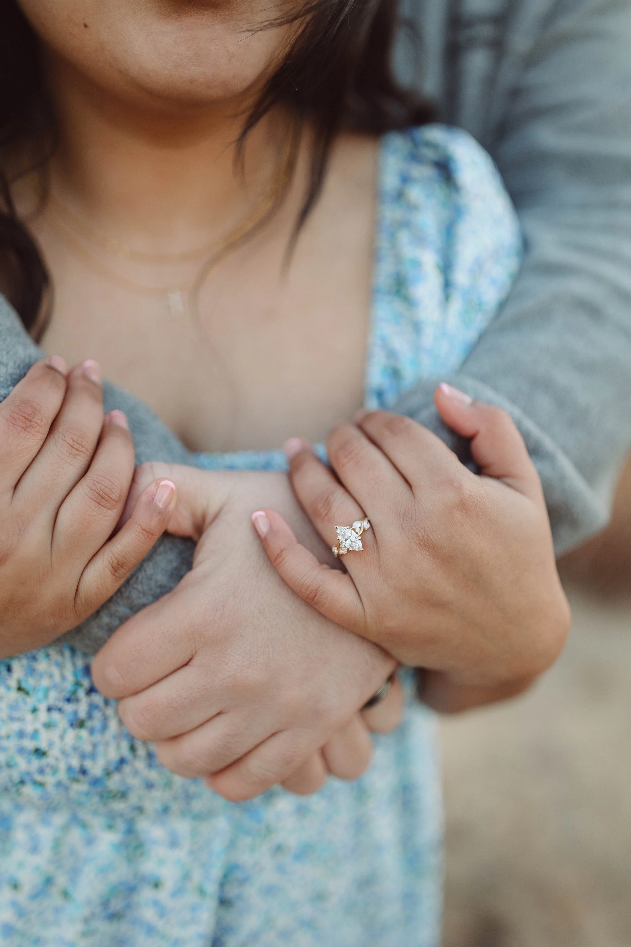 man and woman embrace on sand dunes showing off engagement ring