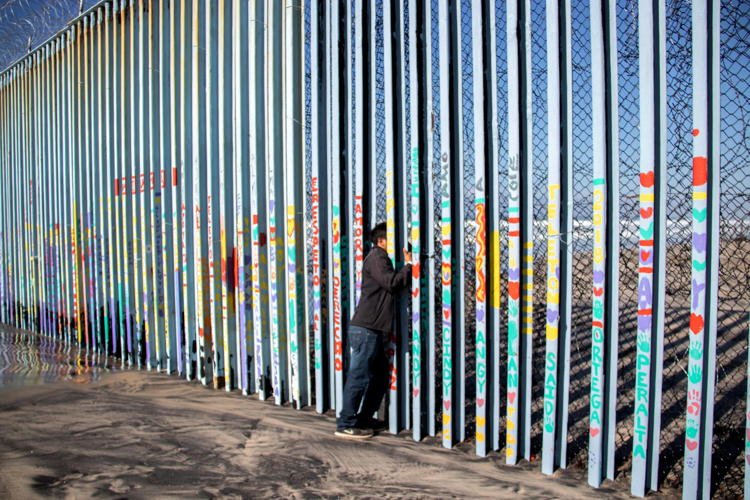  A member of the Honduran Migrant Caravan looks for a gap in the border fence in Tijuana, Mexico.   November, 2018 