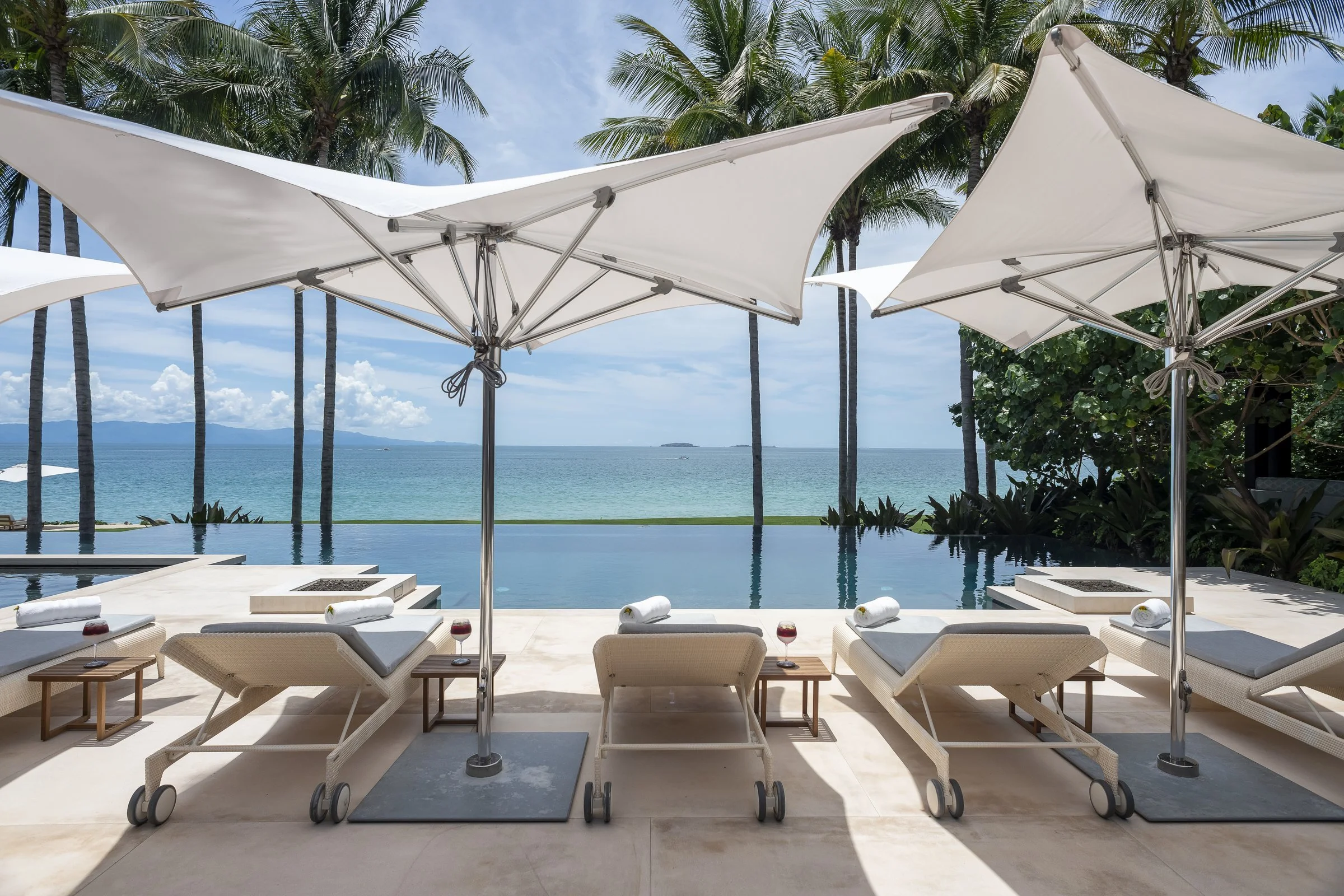 Umbrellas and loungers at the pool's edge, the bay over the vanishing edge