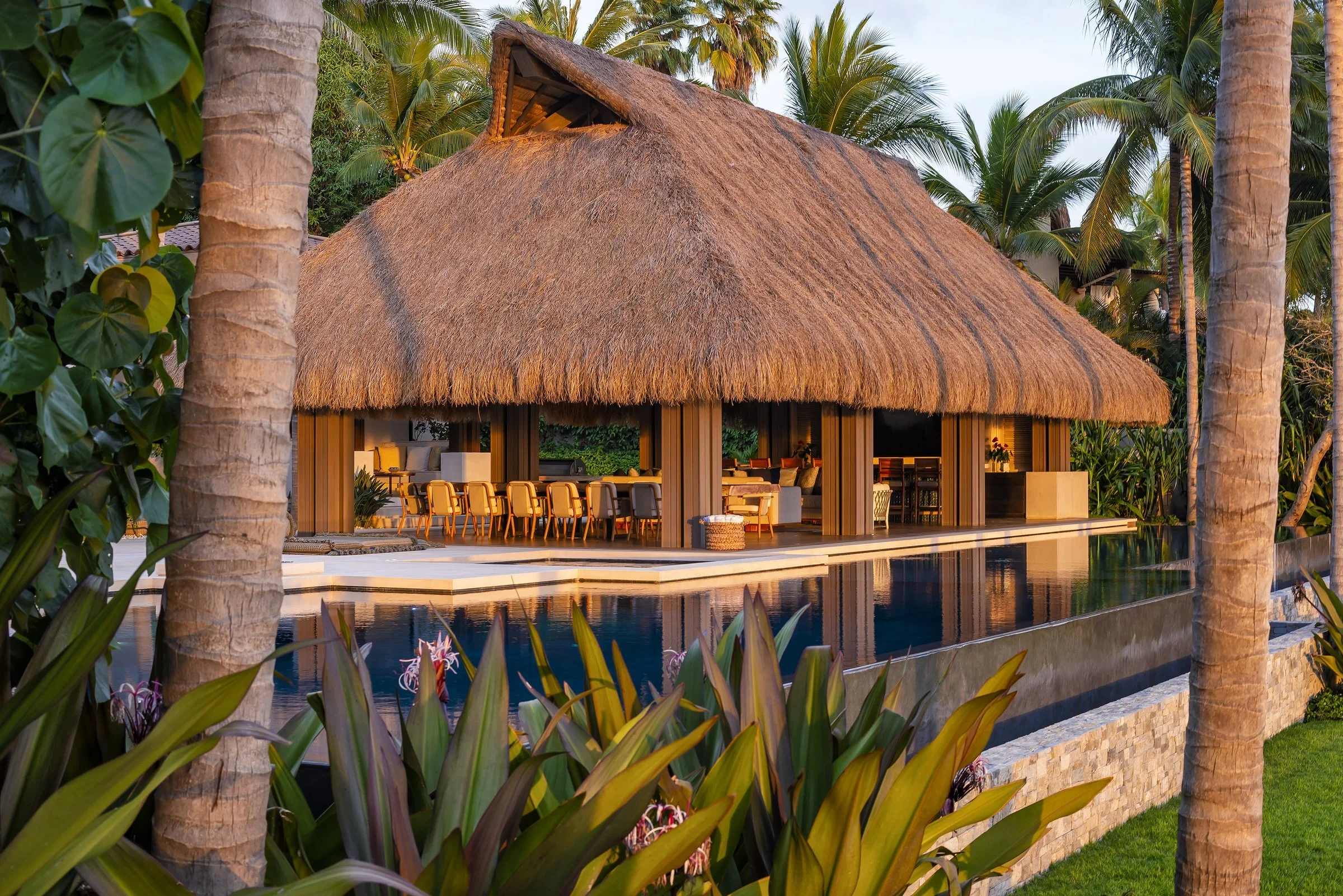 The main palapa glowing gold across the pool at dusk