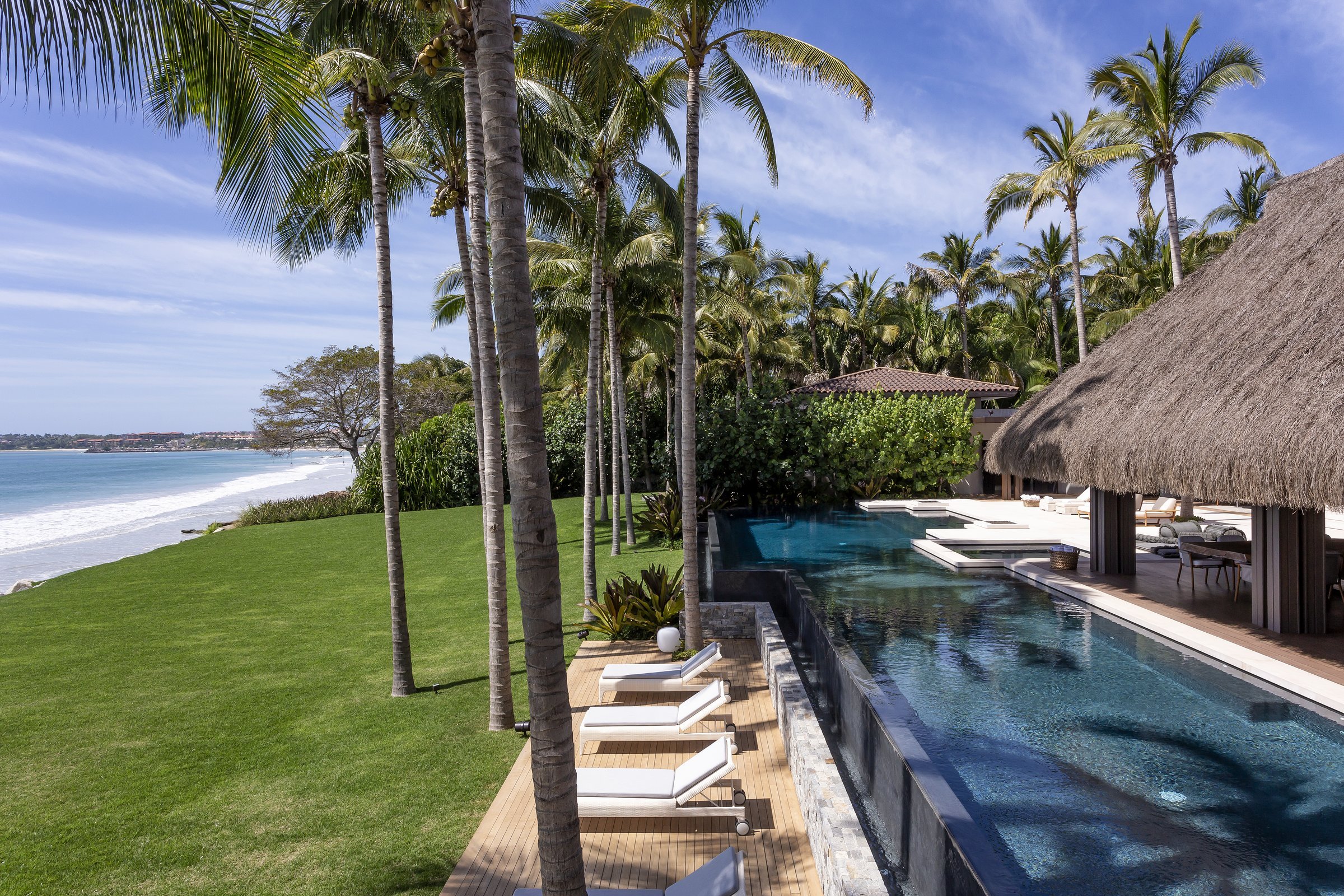 The 130-foot main pool running along the lawn's edge, the beach beyond