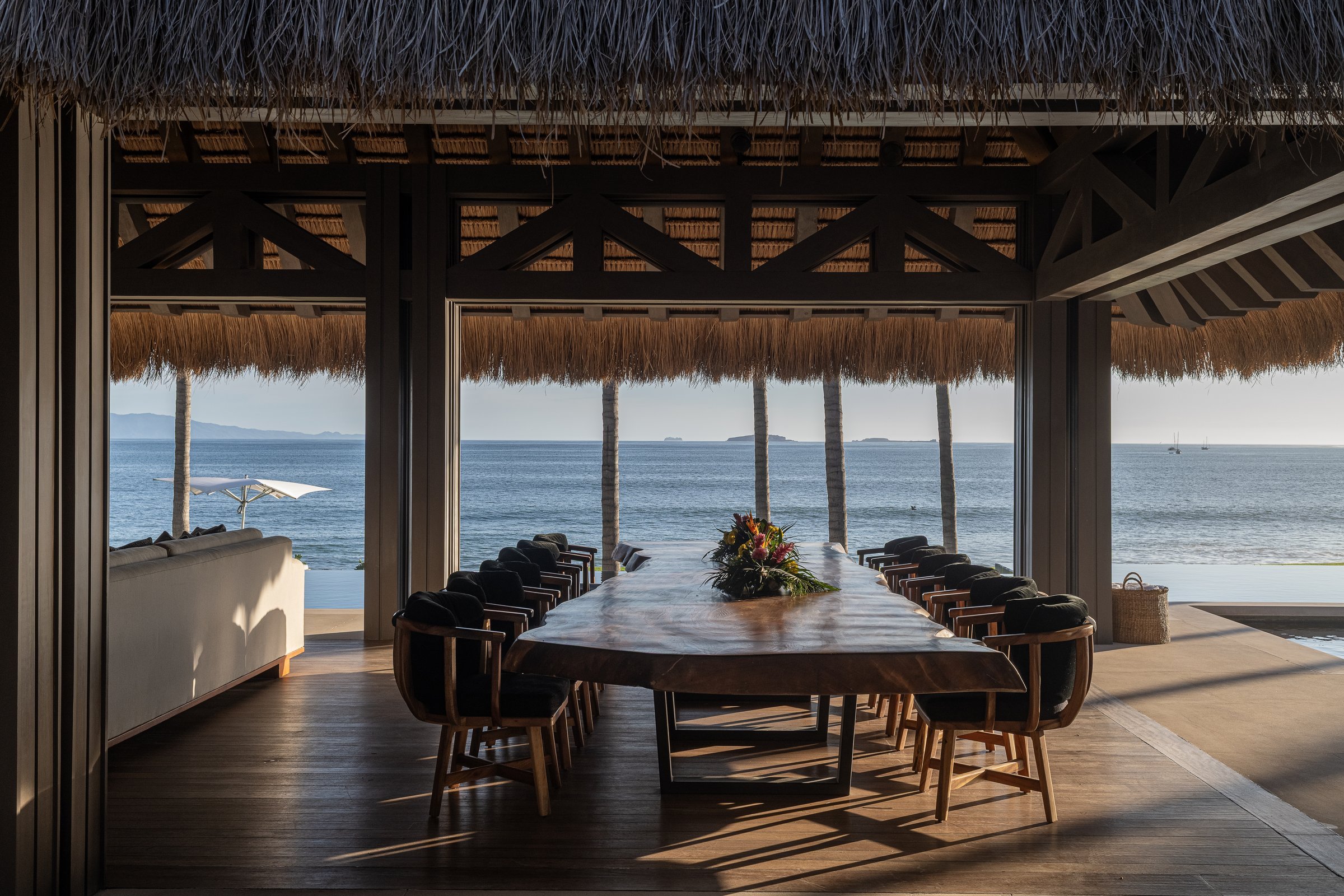 The live-edge palapa dining table set for twenty, ocean beyond