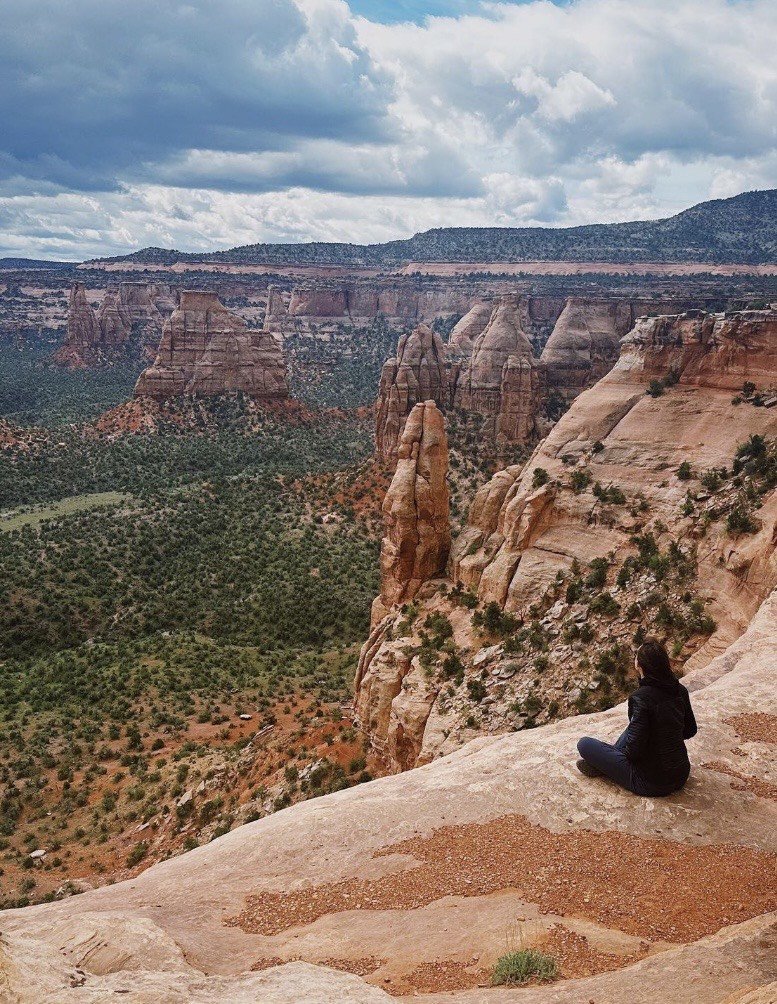 The wild west, frontier for inner wisdom, a  person sitting on a rocky ledge overlooking the red rock formations of a canyon under a cloudy sky.