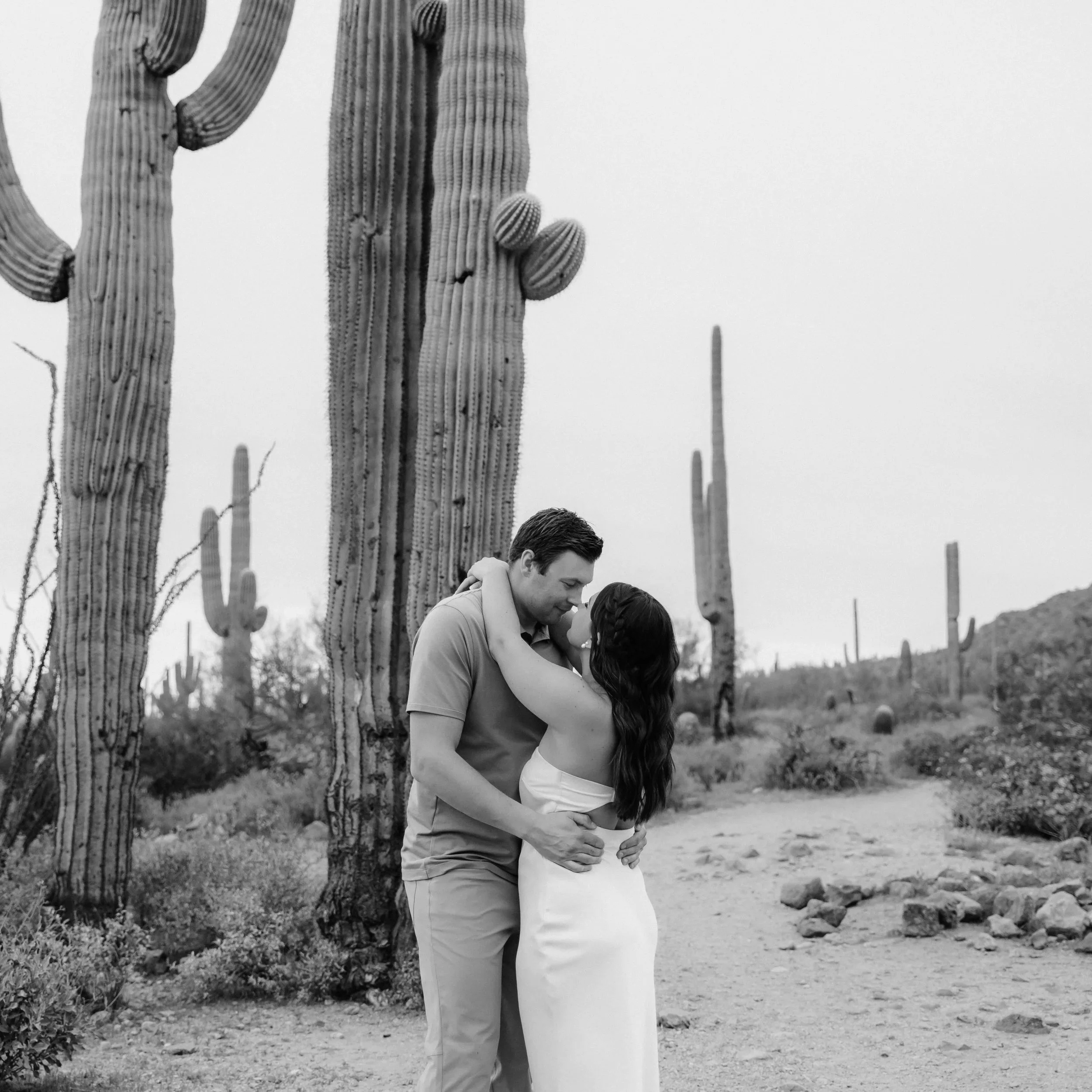 A couple embracing in a desert landscape with tall saguaro cacti.