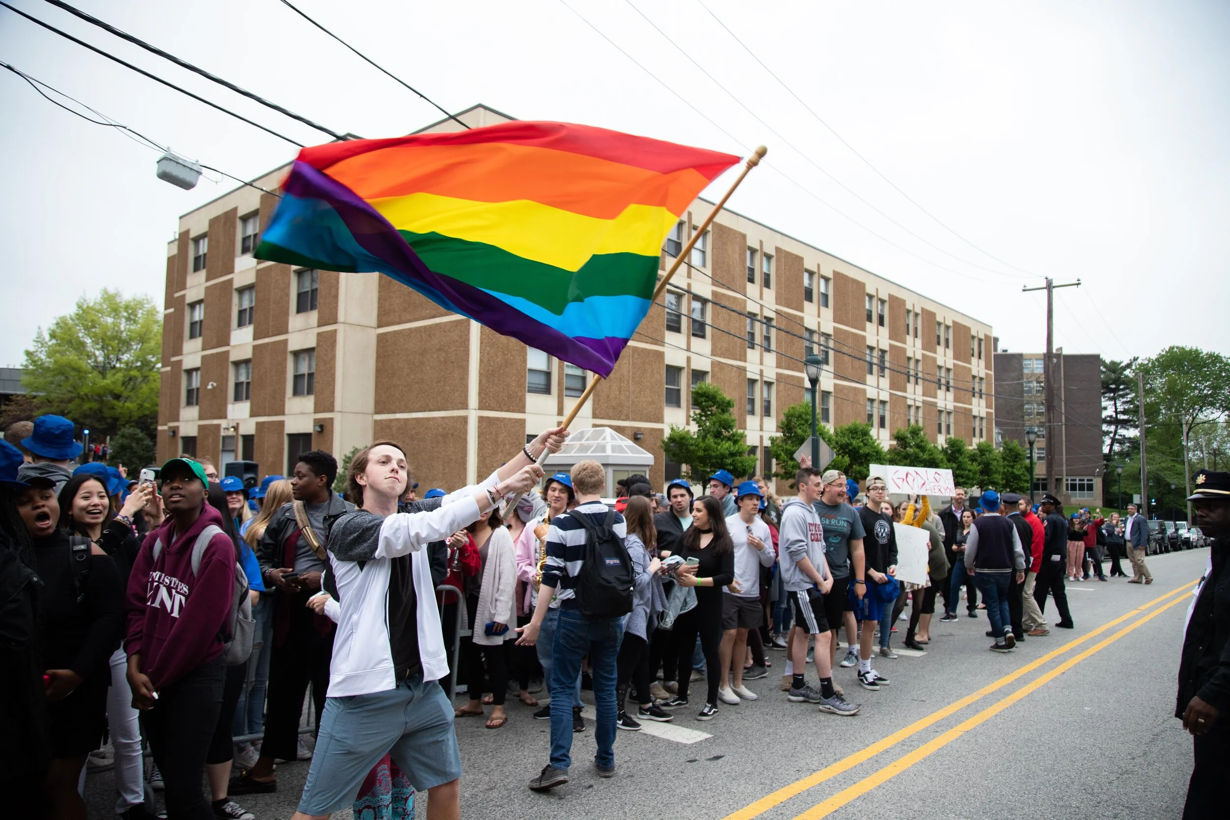   Liam O'Neil '20, member of SJU Pride, waves a rainbow flag at a counter-protest against a group of protesters protesting against  LGBTQ  rights, among other things. Photo for The Hawk News.  