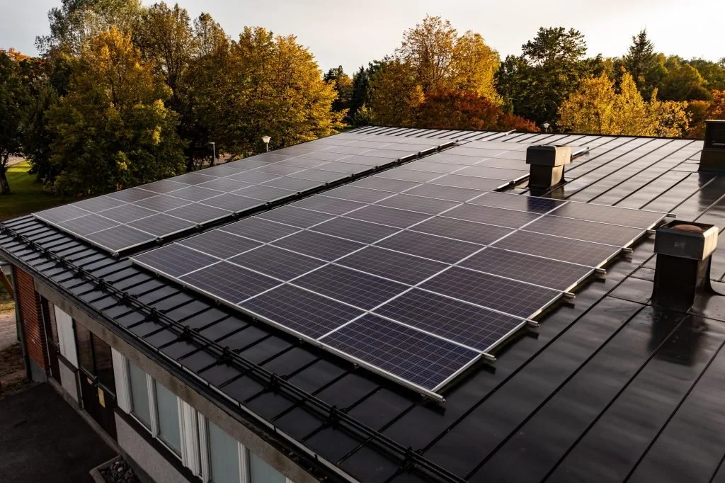 Rooftop with multiple solar panels installed amidst trees with fall foliage.