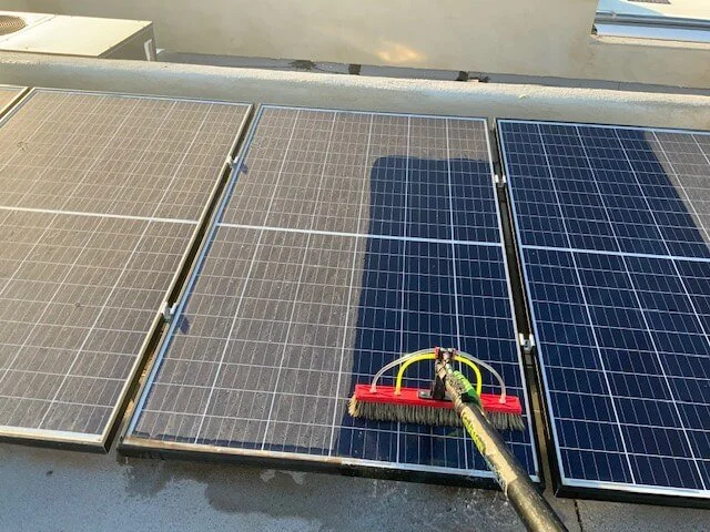 Cleaning solar panels with a broom attached to a long pole on a rooftop.