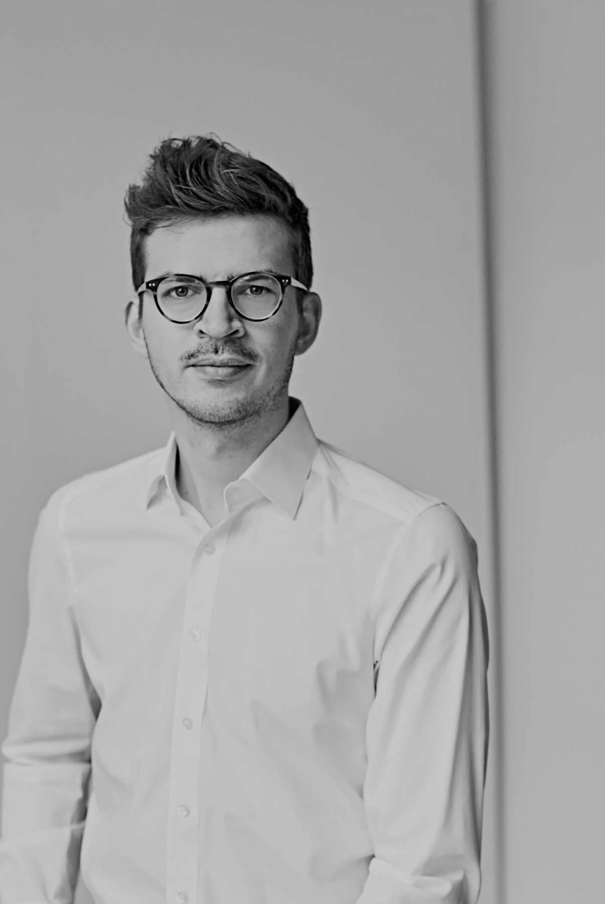 Schwarz-weiß-Foto eines Mannes mit Brille, weißem Hemd, lächelnd, vor neutralem Hintergrund. Professionelle Bewerbungsfotos im Fotostudio in Hannover
