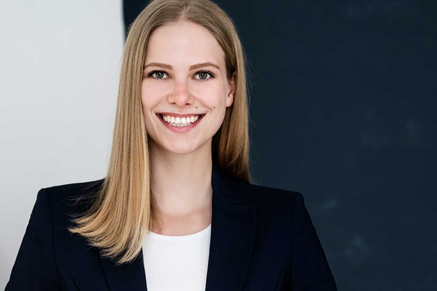 Ein lächelndes junges Mädchen mit langem blondem Haar in professioneller Kleidung vor einem zweifarbigen Hintergrund. Professionelle Bewerbungsfotos im Fotostudio in Hannover