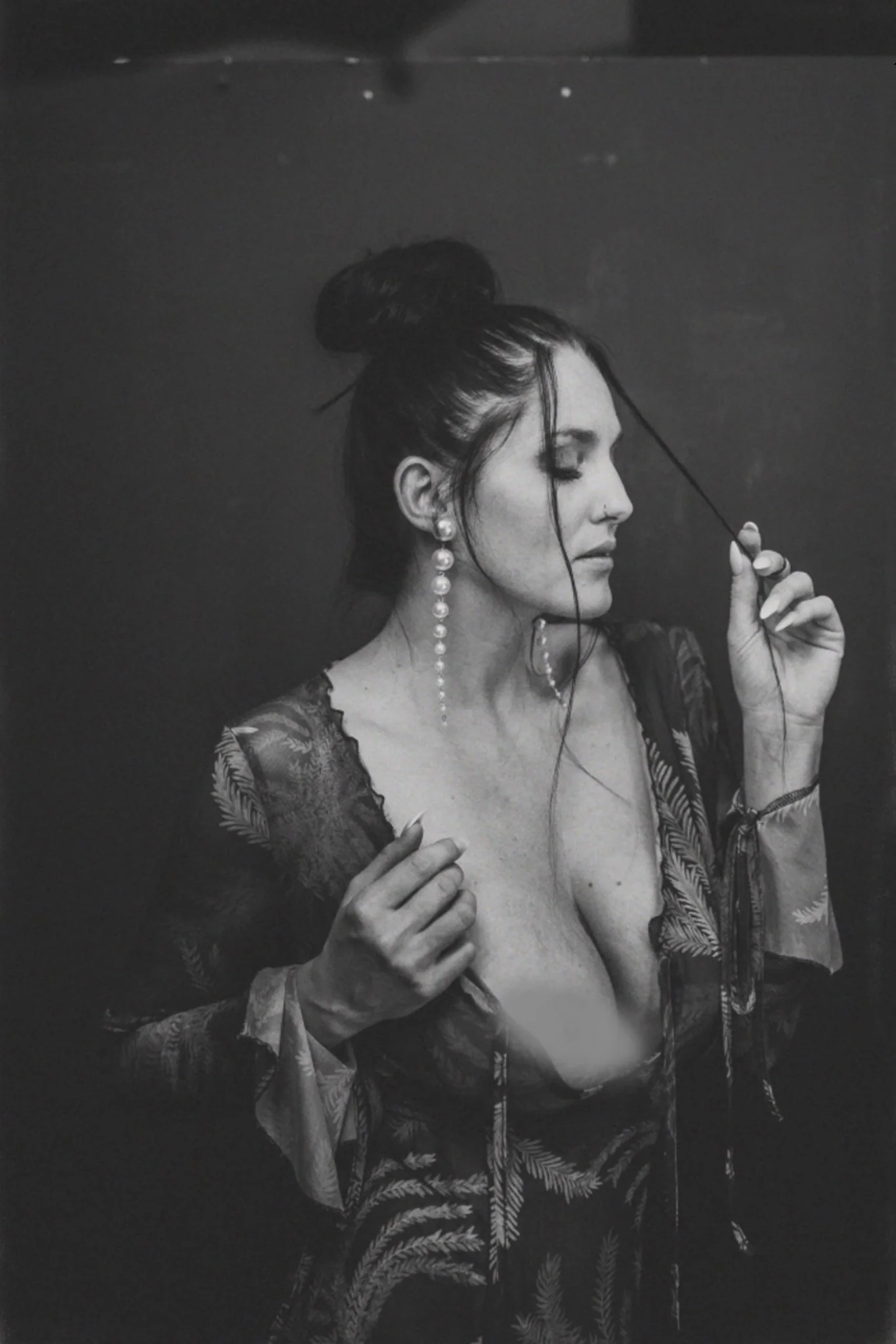 Schwarz-Weiß-Fotografie einer Frau mit Hochsteckfrisur, Perlenohrschmuck und off-shoulder Kleid, die eine lockige Jacke trägt und ihre Haare trocknet.