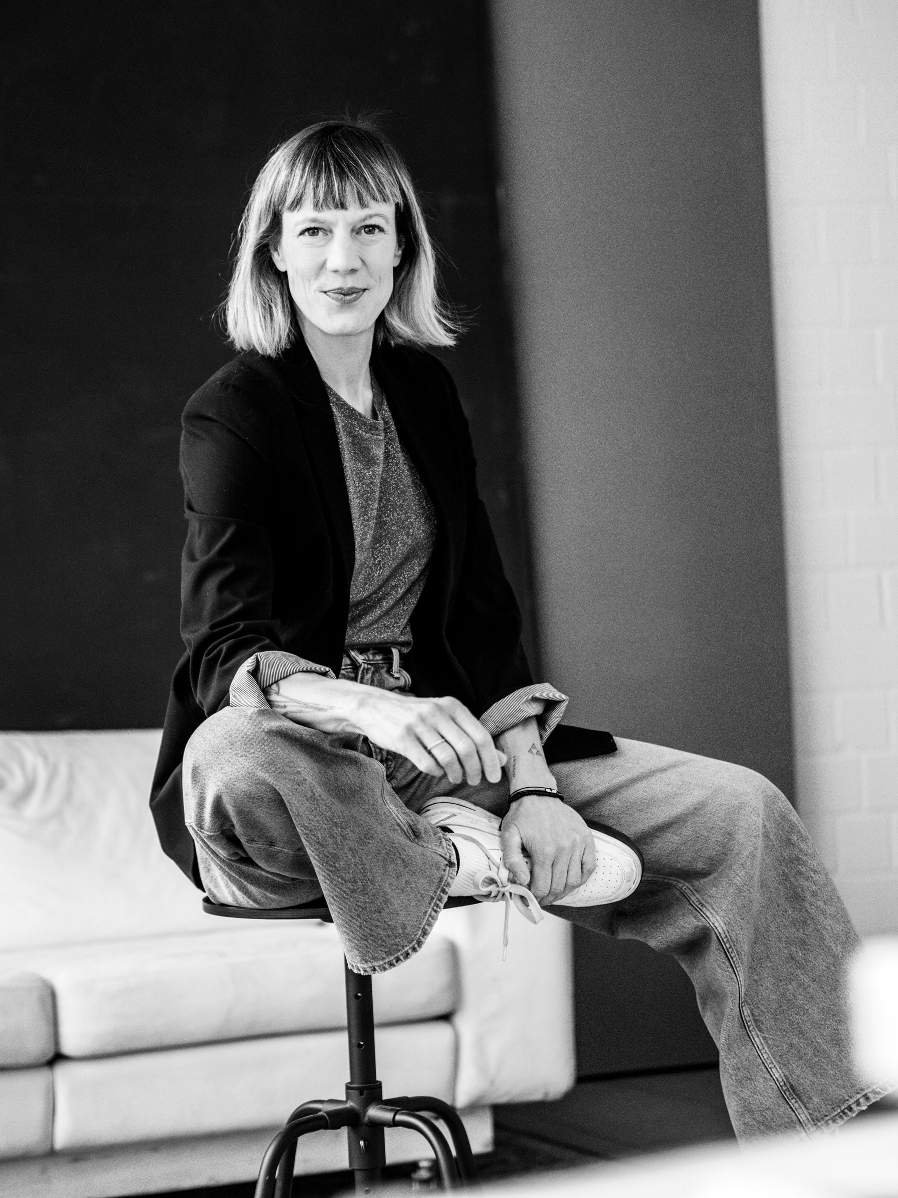 Schwarz-weiß-Foto eines lachenden Mannes, der auf einem Stuhl sitzt, mit einer Frau auf seinem Schoß, die ihre Arme um ihn gelegt hat, in einem Raum mit Sofa im Hintergrund. Professionelle Bewerbungsfotos im Fotostudio in Hannover