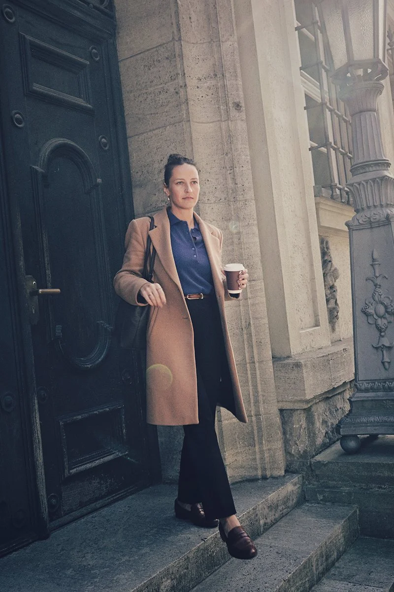 Eine Frau steht vor einem alten Gebäude und hält einen Kaffeebecher in der Hand.