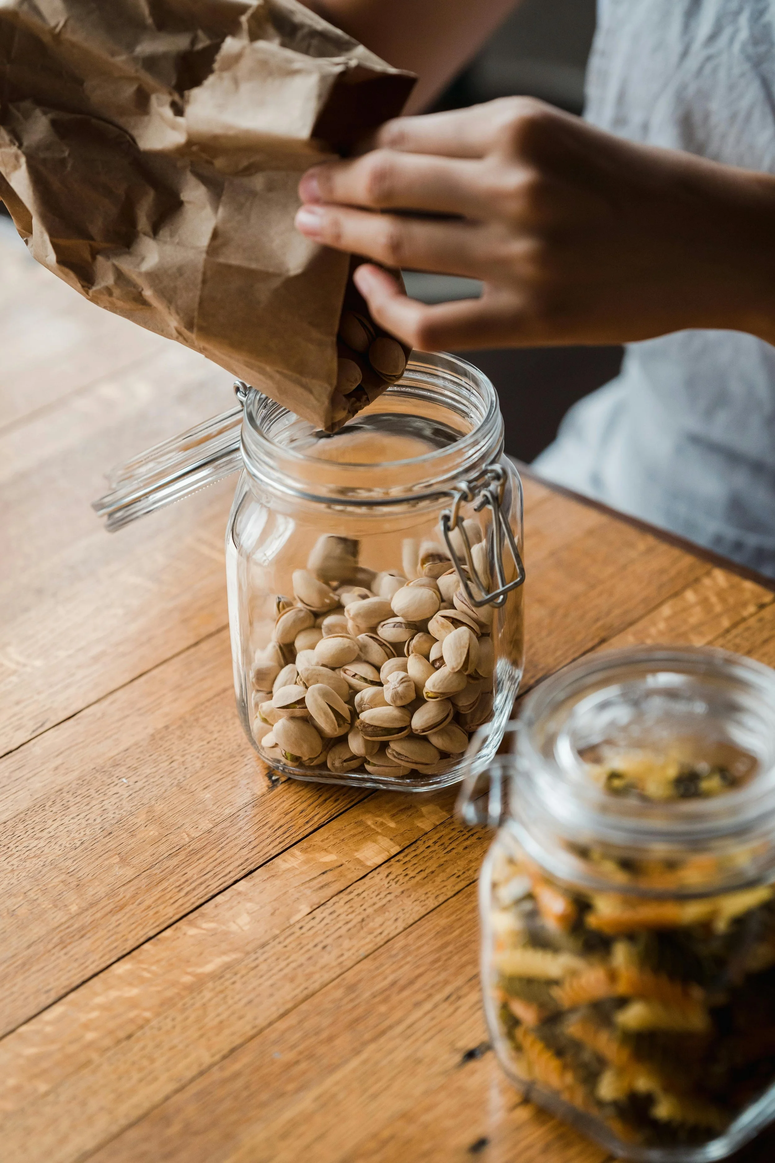 A midlife woman packing healthy travel snacks, including a protein shaker bottle and raw nuts, into her carry-on luggage to maintain nutrition and blood sugar while traveling