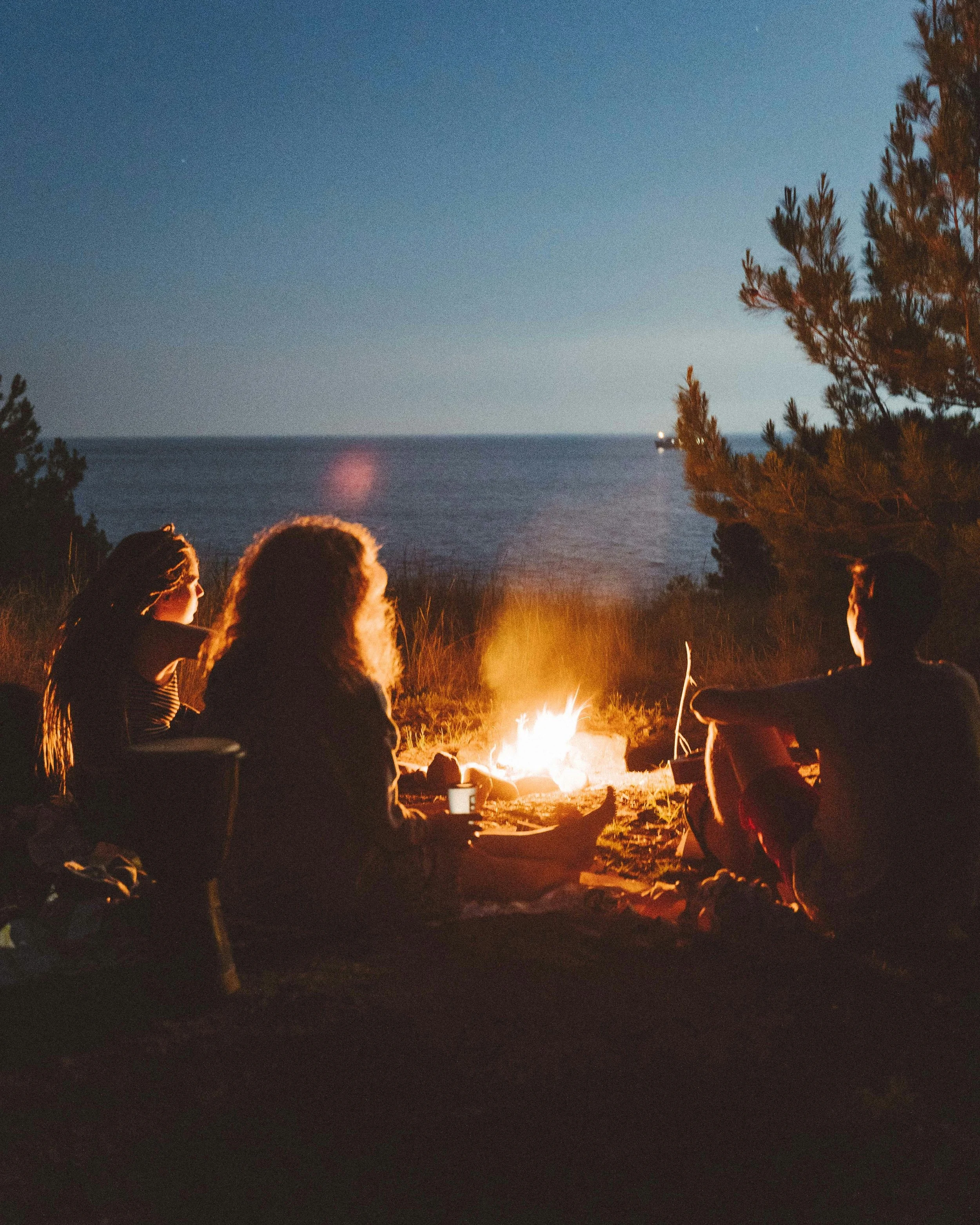 A diverse group of women in their 40s and 60s sharing a conversation around an evening campfire.