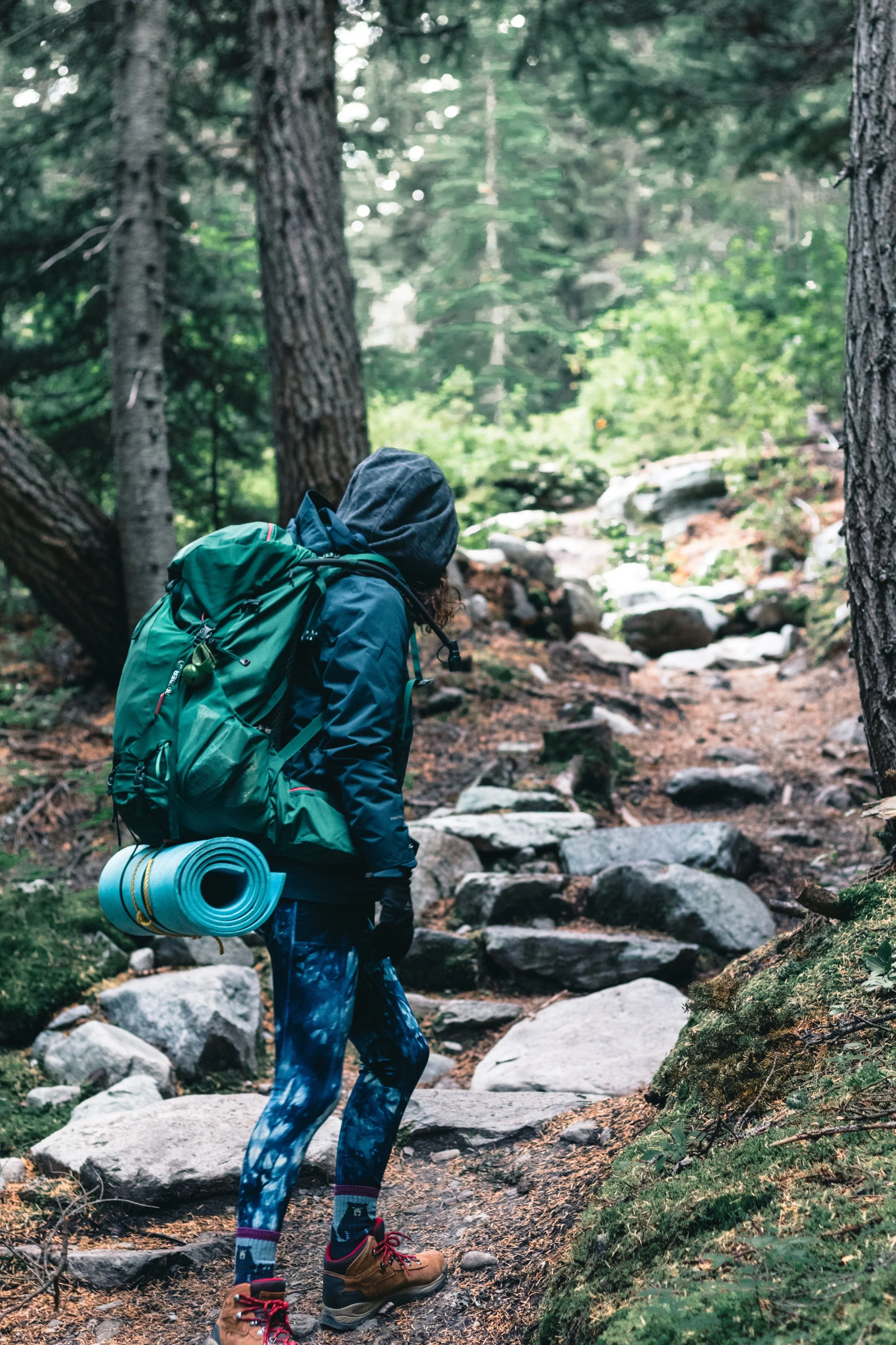 A woman hiking on a wooded trail wearing protective clothing with her pants tucked into tall socks to prevent tick bites.
