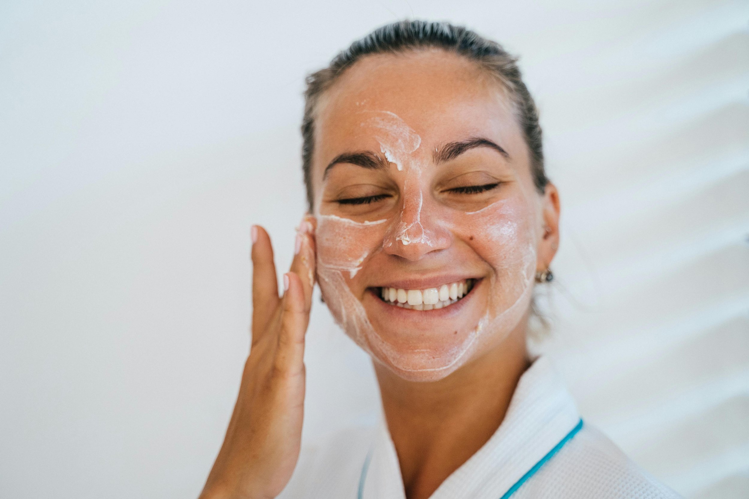 A smiling midlife woman applying a gentle facial moisturizer during her morning routine.