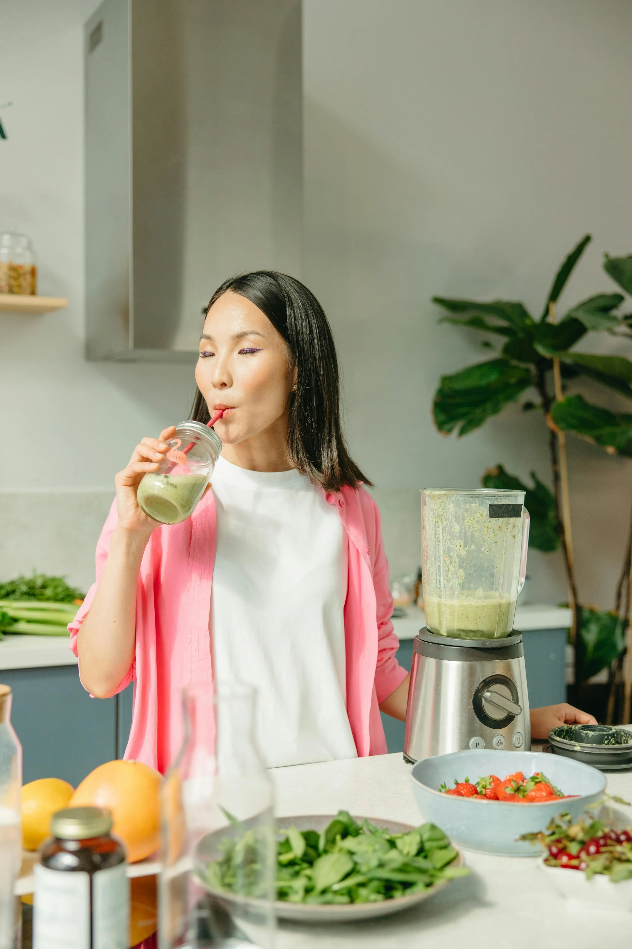 A woman in her 40s smiling while drinking a green wellness smoothie during a midlife liver detox.