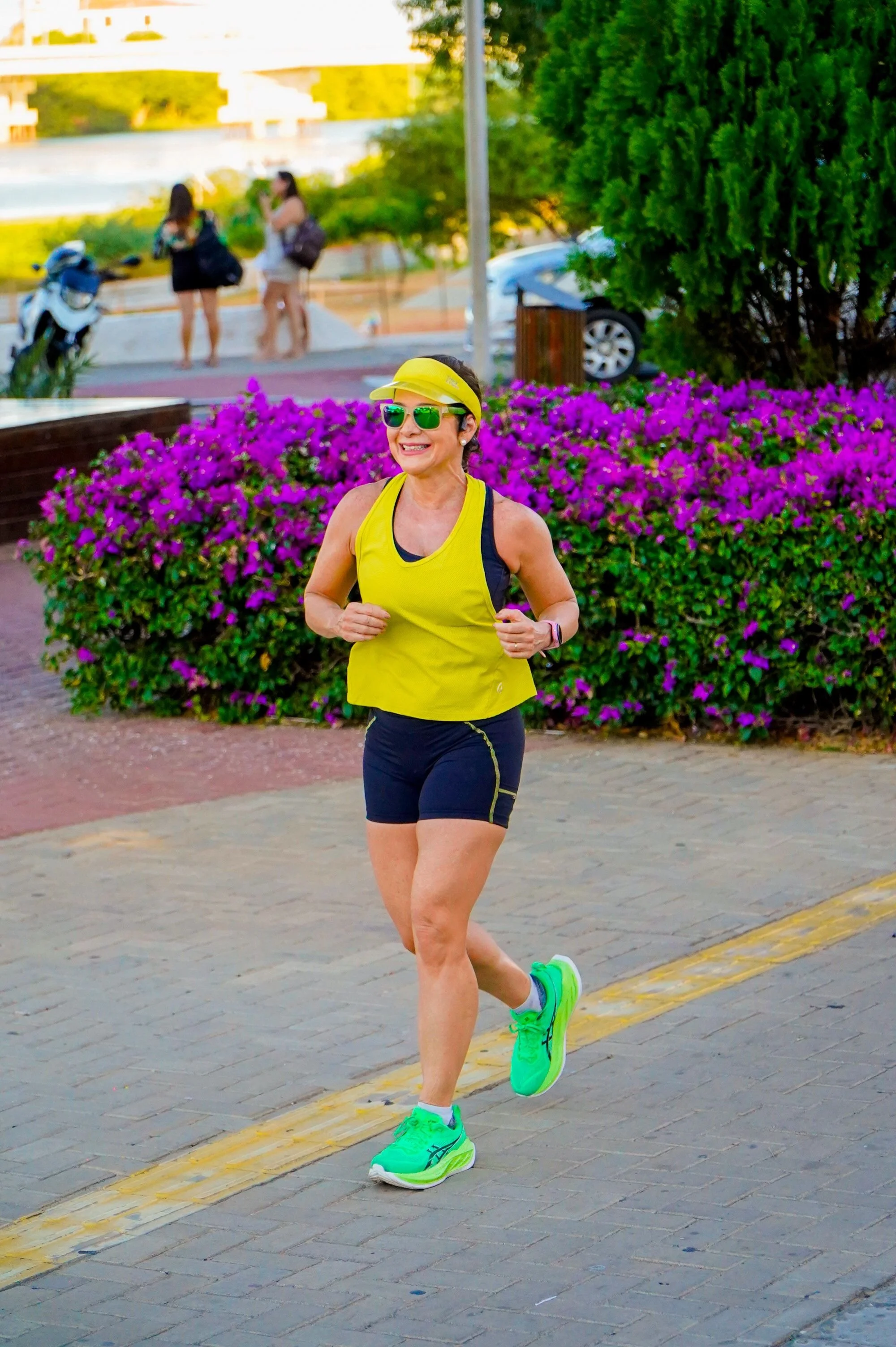 A vibrant, energetic midlife woman smiling while jogging on a sunny outdoor trail.