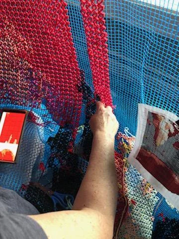 Person working on a pixel art mosaic with various colored tiles, using a tool to place tiles on a grid.