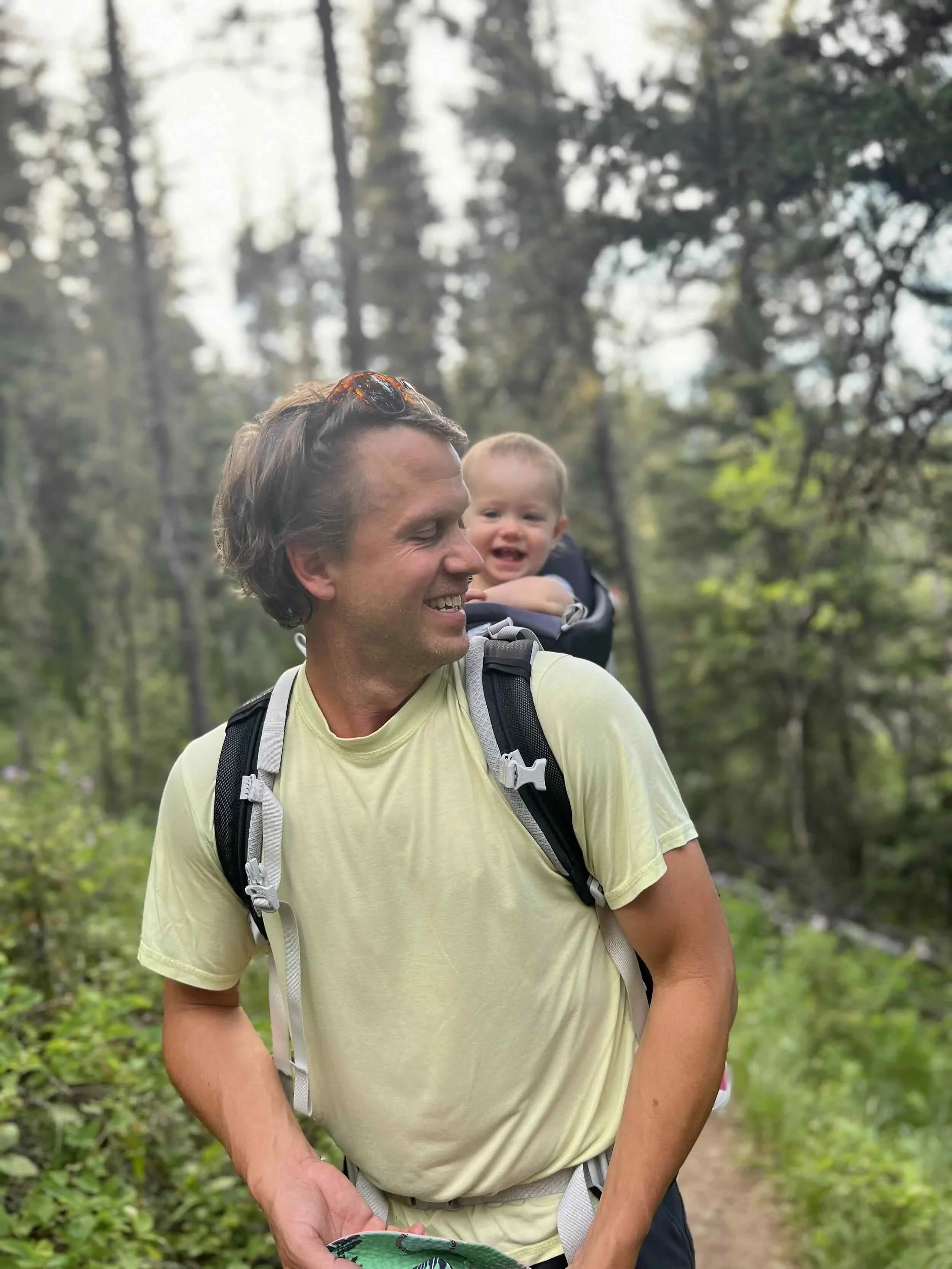 greg hahnel teaching a young girl how to ride a purple and white bicycle with a small white basket in a park during sunset, with yellow fall trees and mountains in the background.