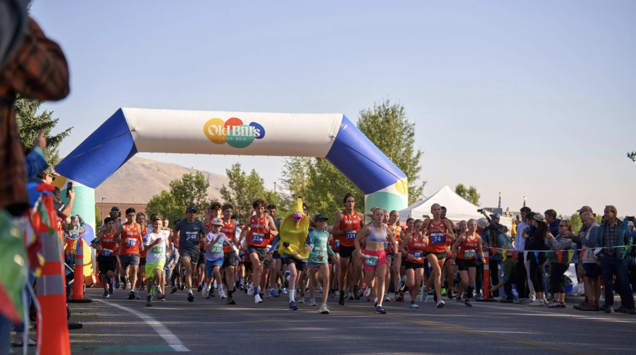A group of kids running through the start line at the Old Bill's Fun Run.