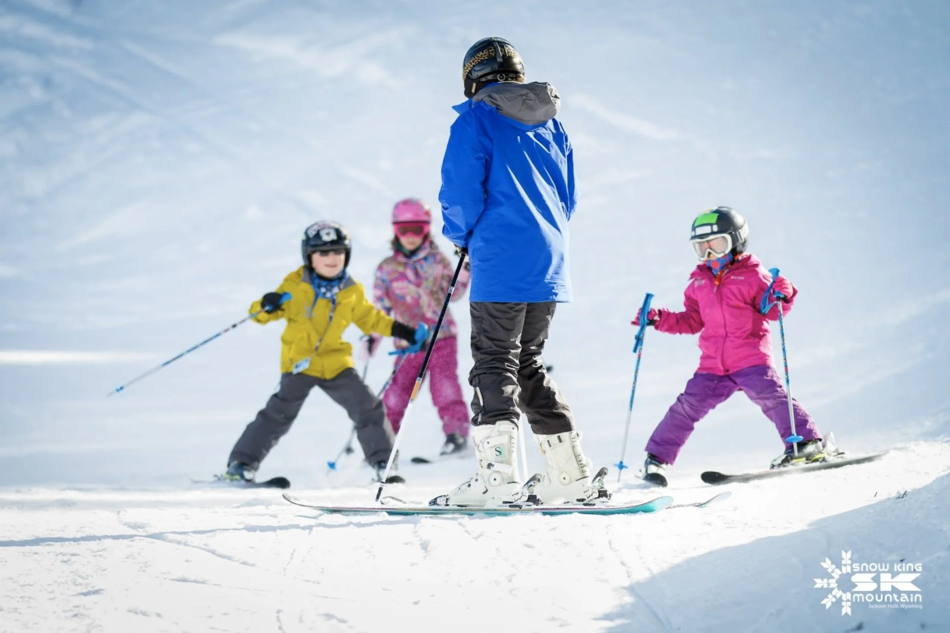 Adult skier teaching three young kids how to ski.