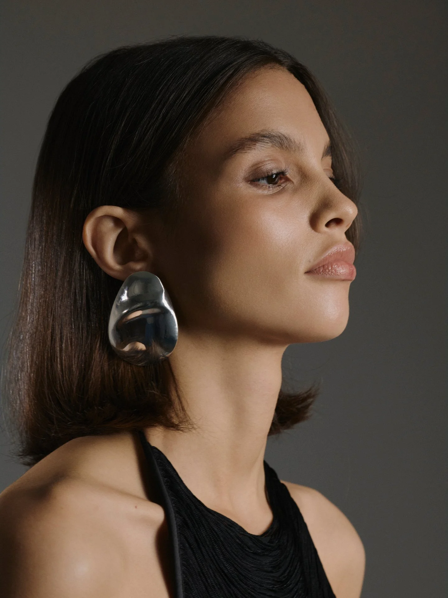 Sculpture for the ear, clarity for the brand. This quiet portrait centres a fluid, silver statement earring against clean lines and skin-lit glow&mdash;proof that one strong form can carry a campaign. At Couture Consultancy, we translate details like