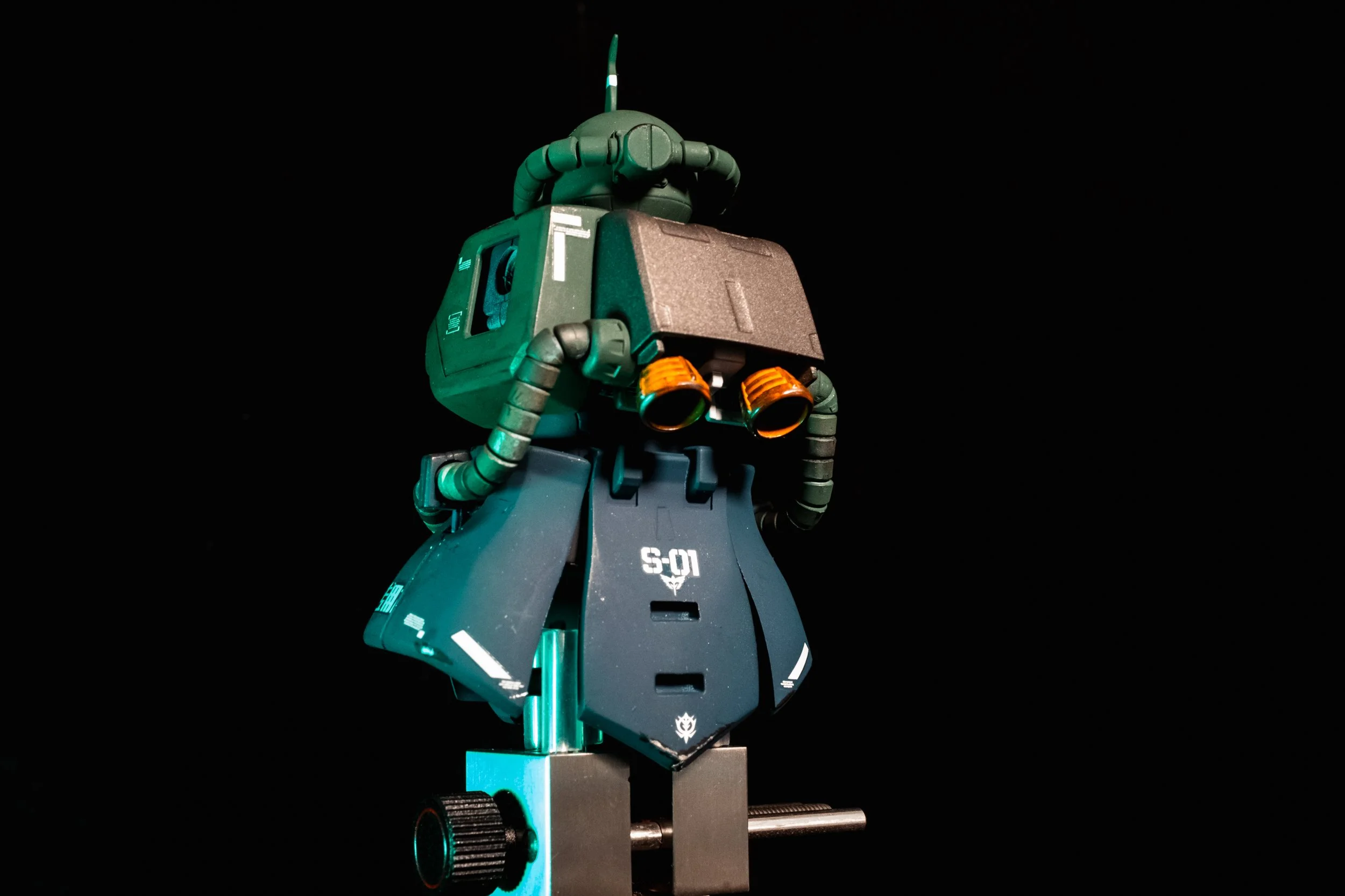 Close-up of a detailed model robot with a green and black color scheme against a black background, showing intricate mechanical and design elements.