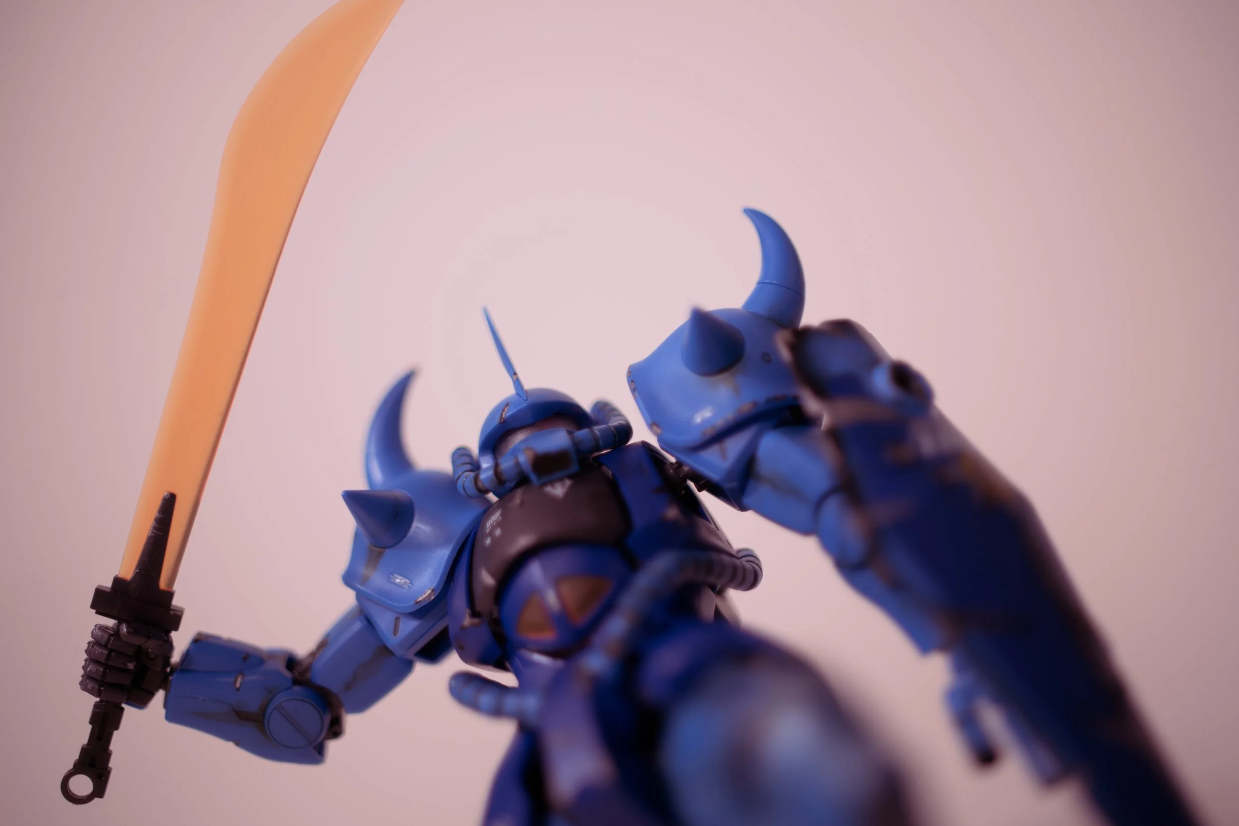 Close-up of a blue armored robot with a sword, shown from below against a plain, light-colored background.