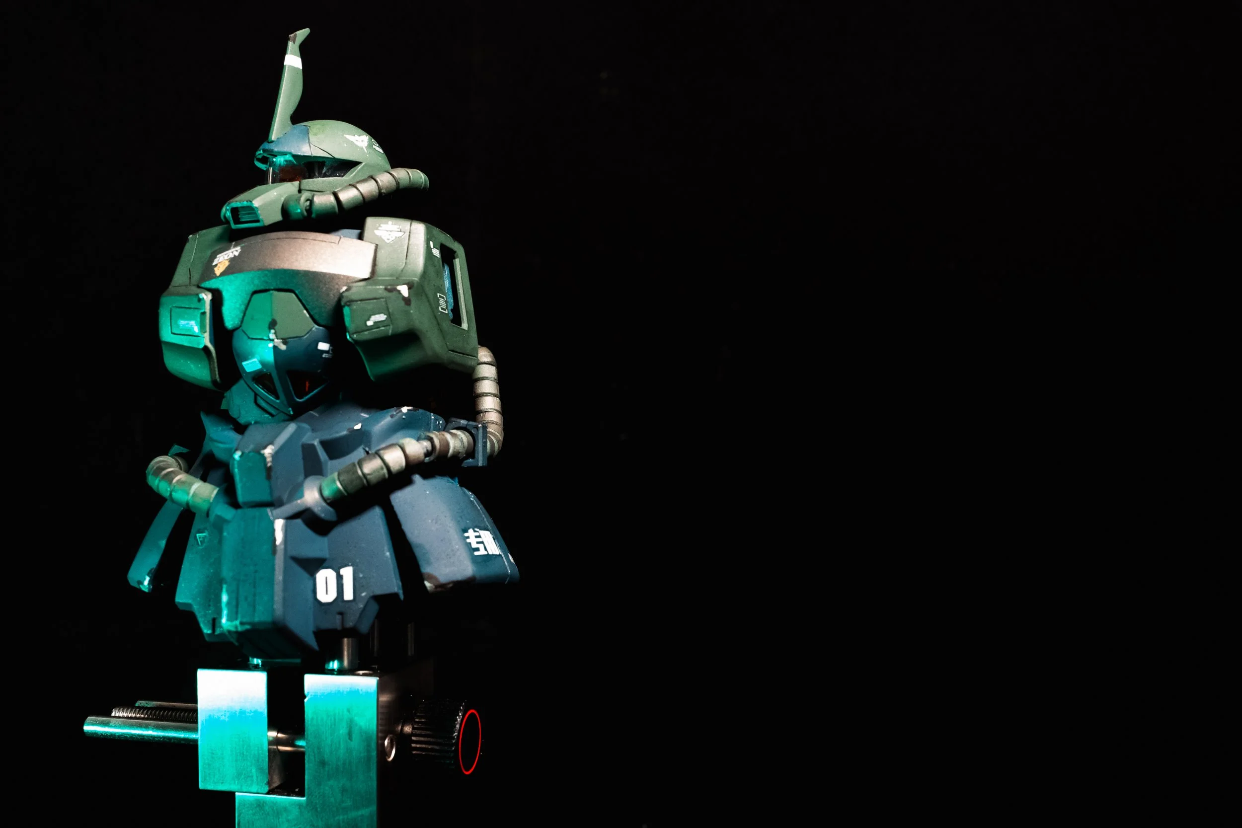 A green color robot figurine on a metallic stand against a black background.