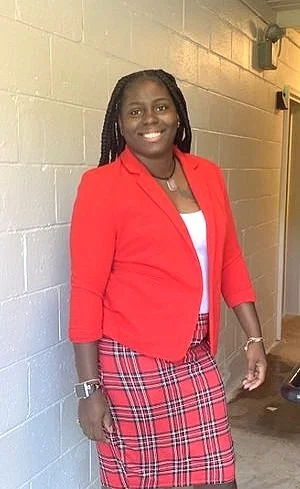 Person wearing a red blazer and plaid skirt, standing in a hallway.