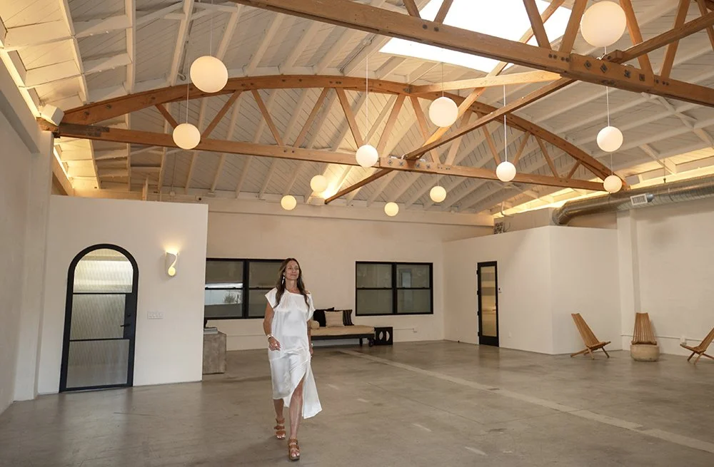 Dre Shapiro founder of Lacuna Space walking through the main interior of Lacuna Space in West Adams Los Angeles featuring exposed wooden roof trusses and globe pendant lights