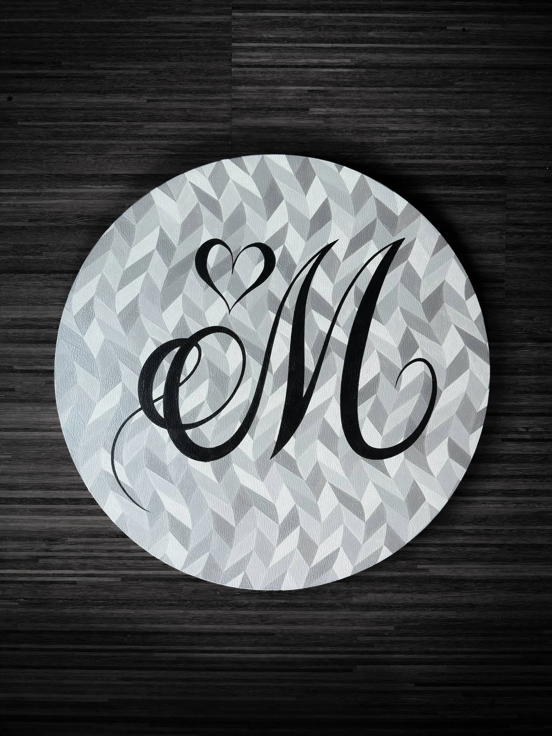 Custom circular calligraphy artwork featuring elegant black scripted monogram over textured geometric silver background