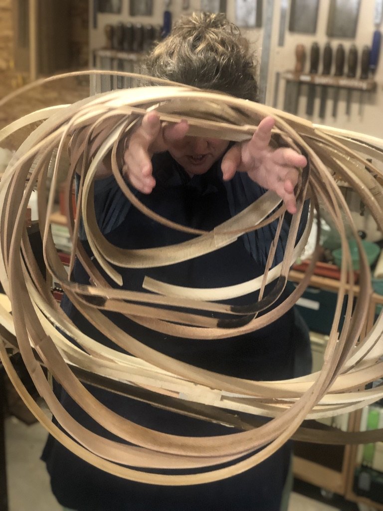 Smiling woman holding a joyful tangle of hot pipe bent timber loops in silver ash, silver quandong and silky oak, in Ross Annels' studio at Coolum Beach