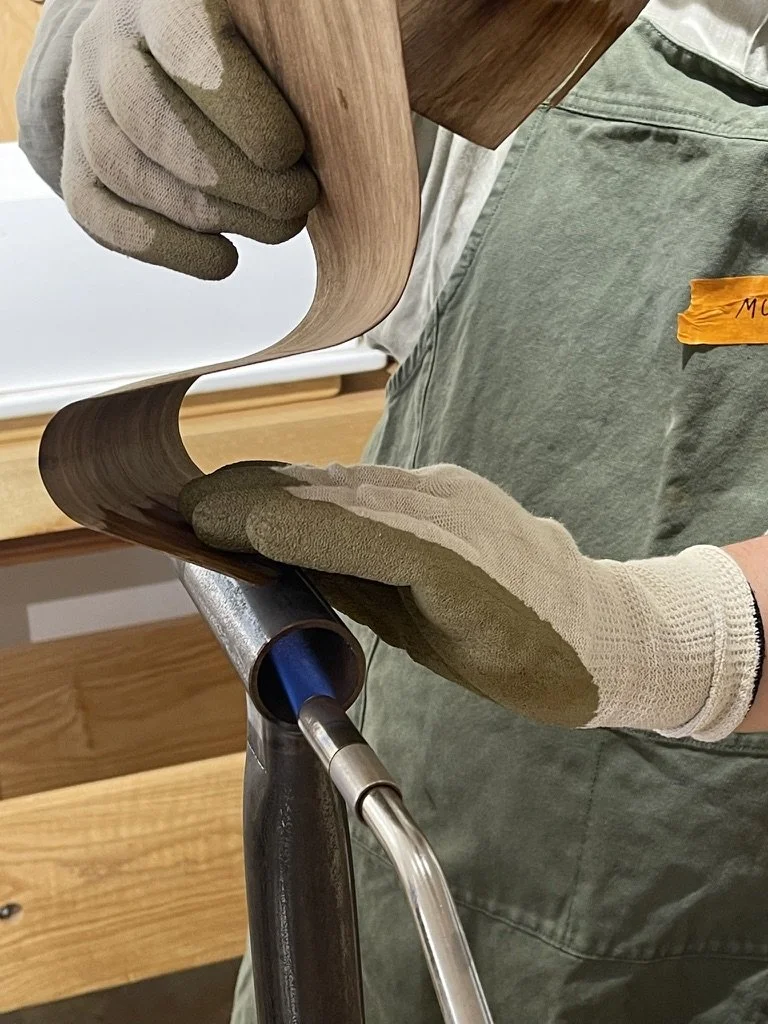 Gloved hands bending a black bean strip over a hot pipe at a workshop with Ross Annels from Moonlite Studios