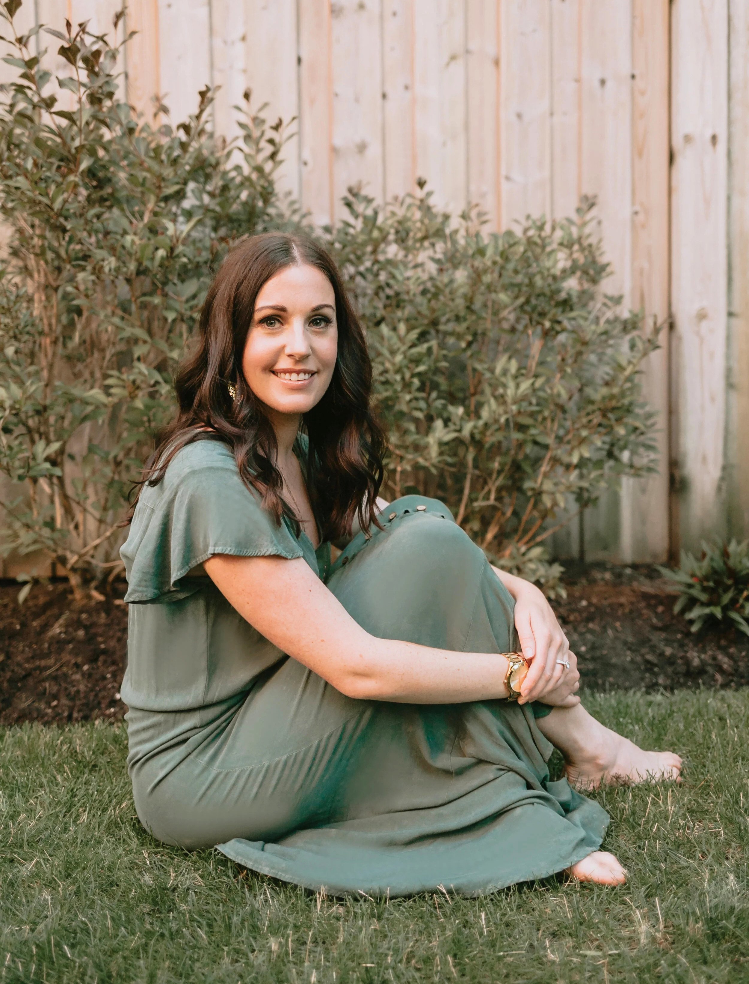 Woman in long green dress sitting a grassy fenced yard