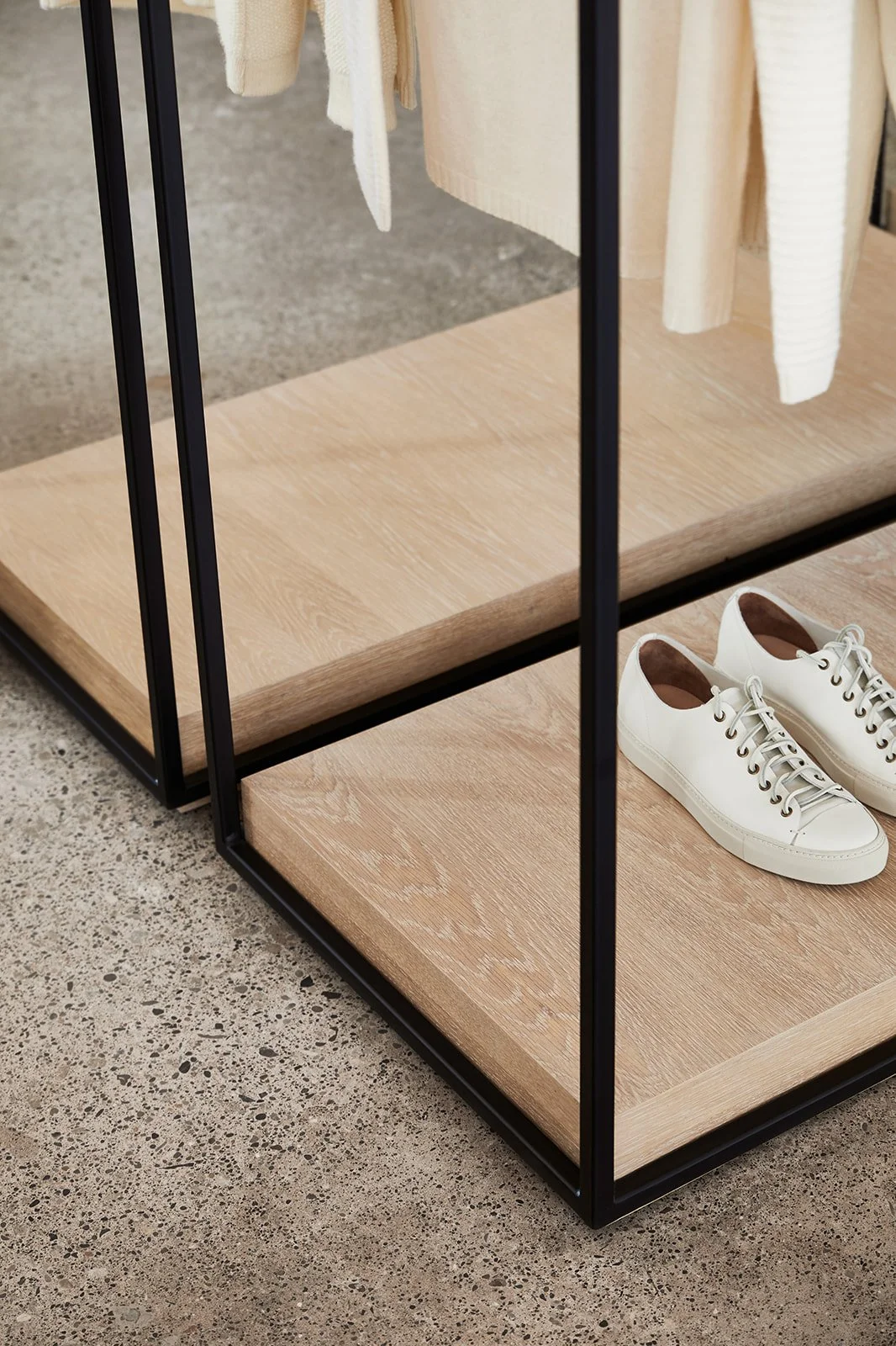 A retail display case with a black metal frame and wooden shelves, showcasing a pair of white sneakers.