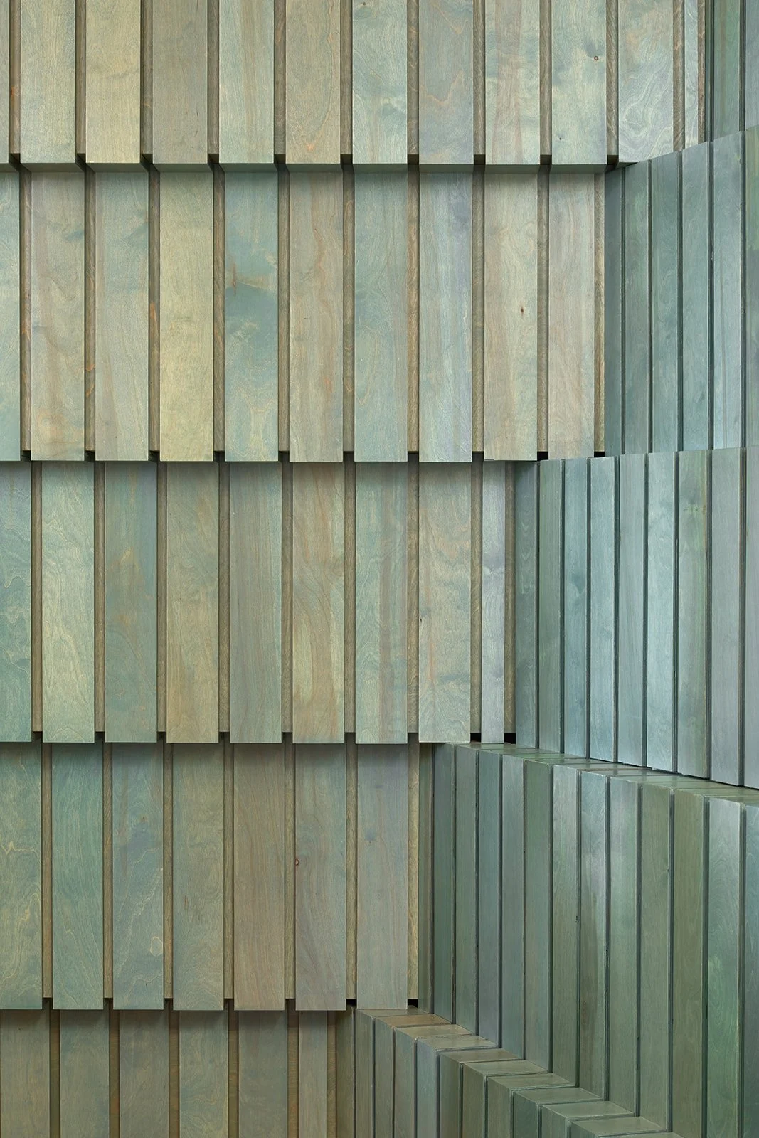 Stacked wooden planks painted in shades of green and blue, forming a corner.